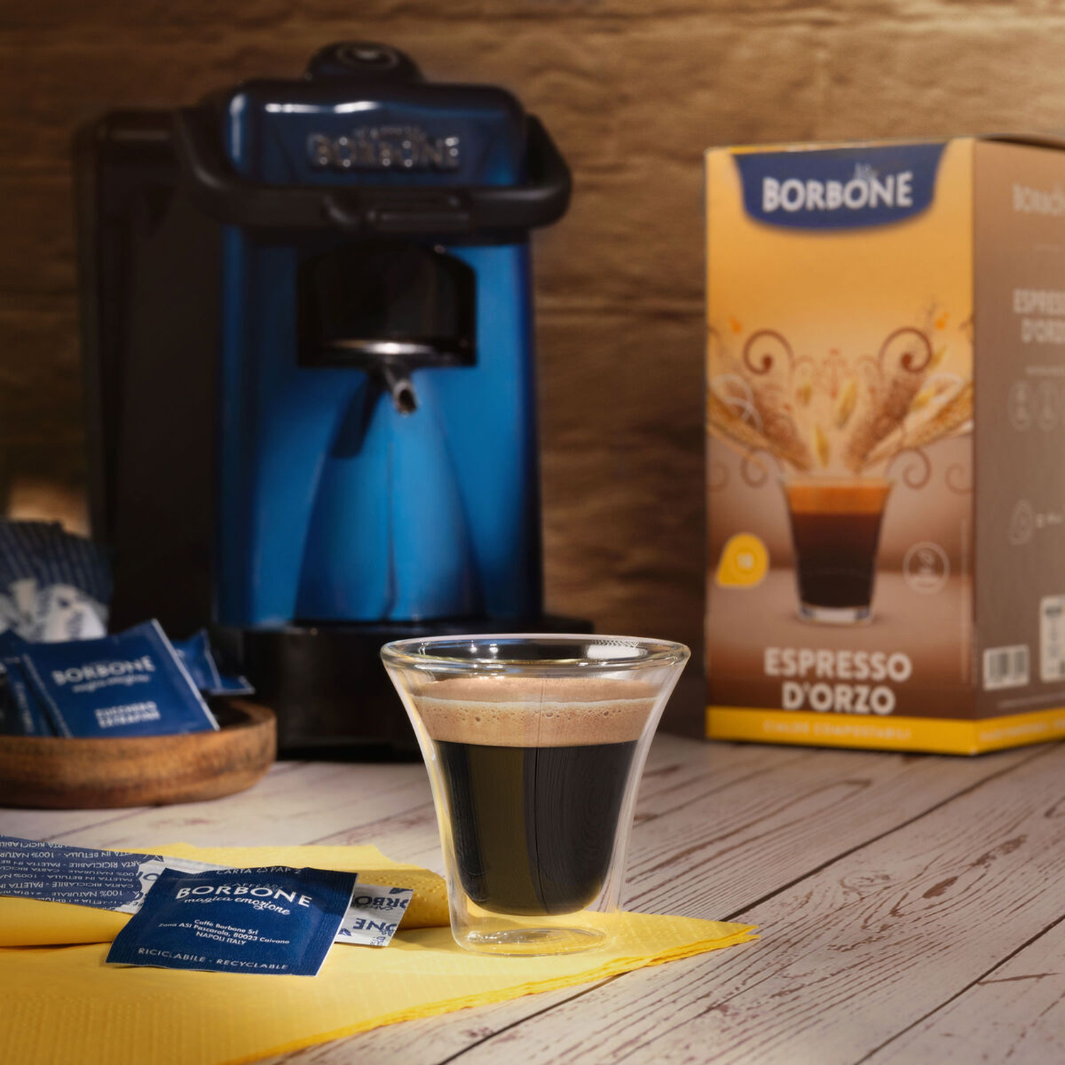 Una macchina da caffè blu, una scatola e un bicchiere di espresso su un tavolo di legno.