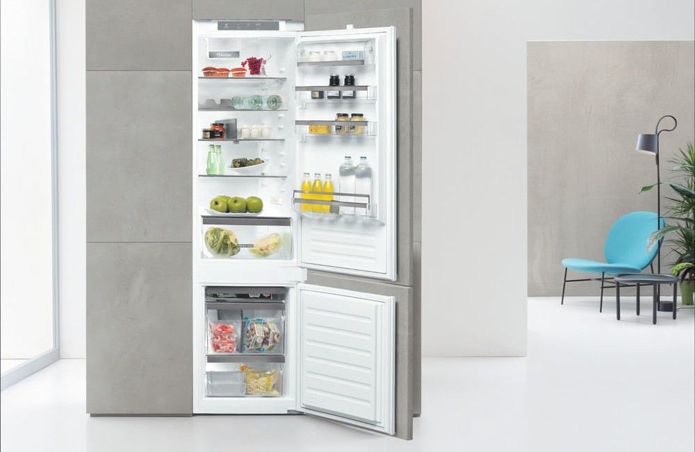 Un refrigerador abierto con comida y un área de sillas azules.