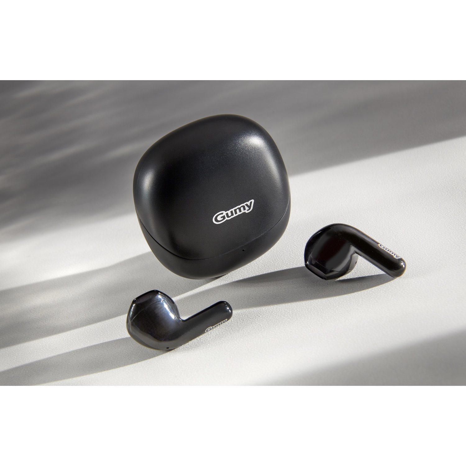 Auricolari wireless Gummy neri e custodia di ricarica su superficie bianca.