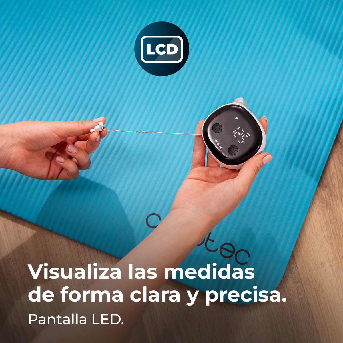 Una mano sostiene un medidor con pantalla LCD sobre una alfombrilla azul.
