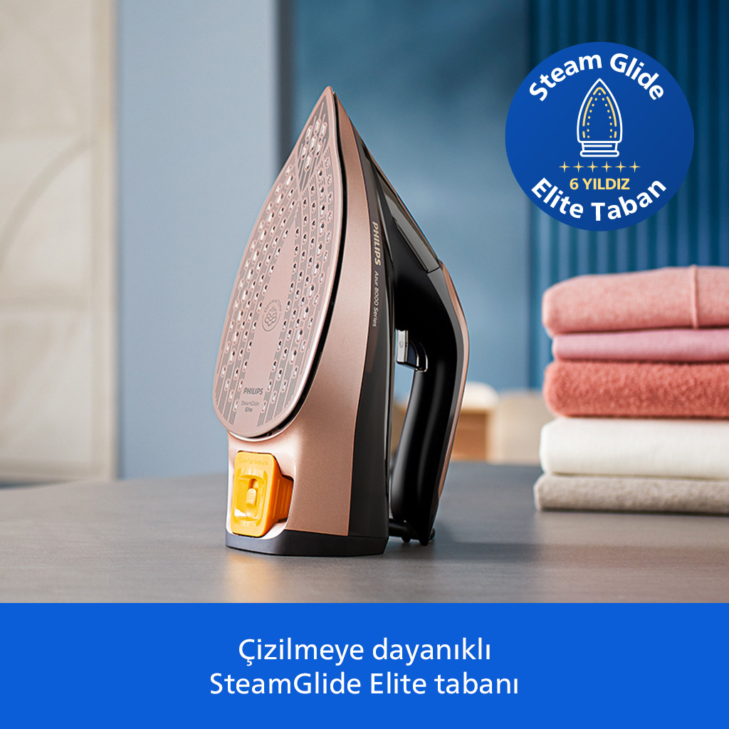 Gül altın rengi buharlı ütü masada duruyor. Yakınında havlu yığını var.