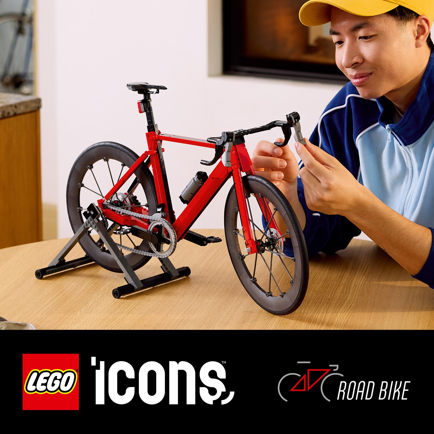 Un uomo assembla una bici da corsa Lego rossa su un tavolo.