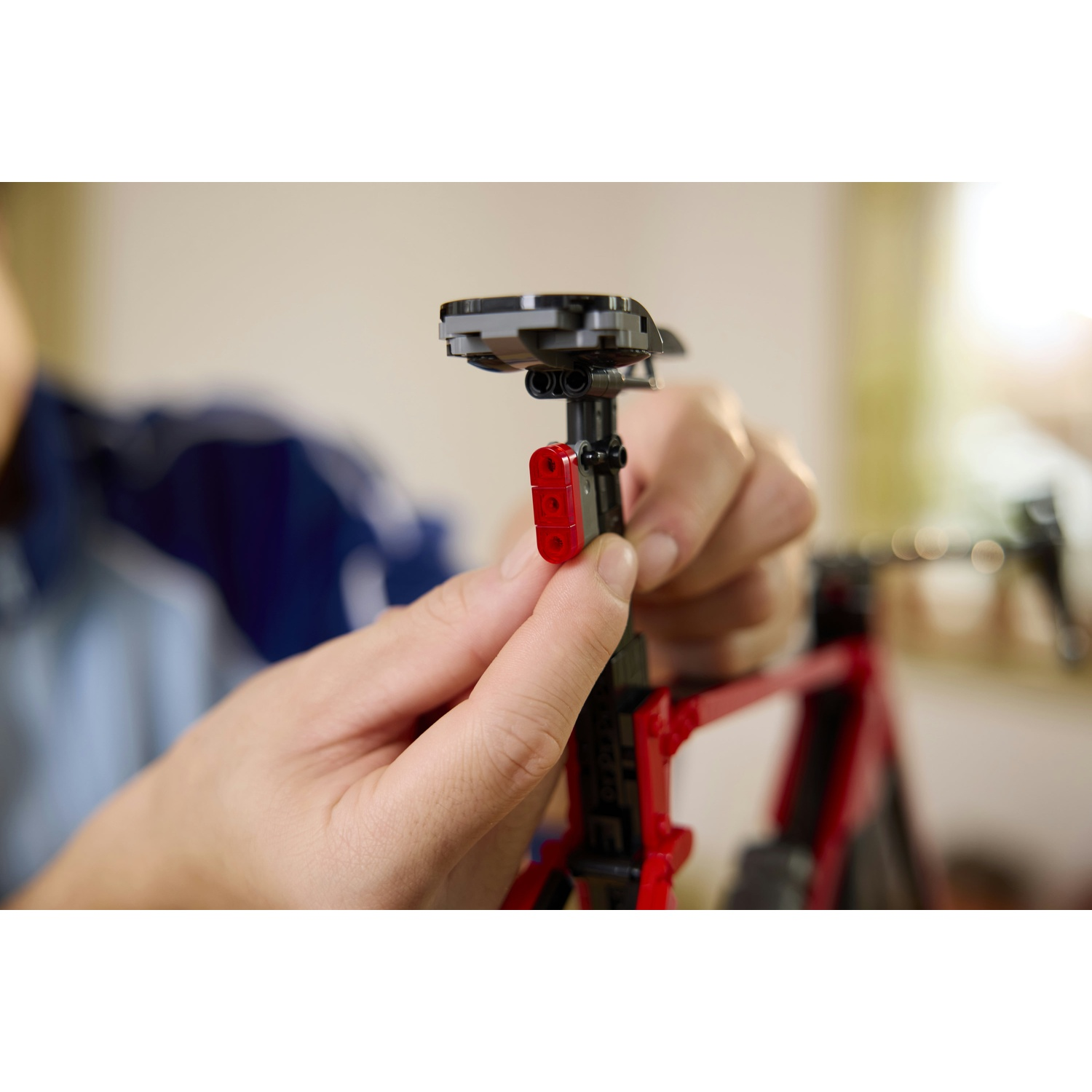Mani assemblano un telaio di bicicletta Lego rosso con un sedile nero.