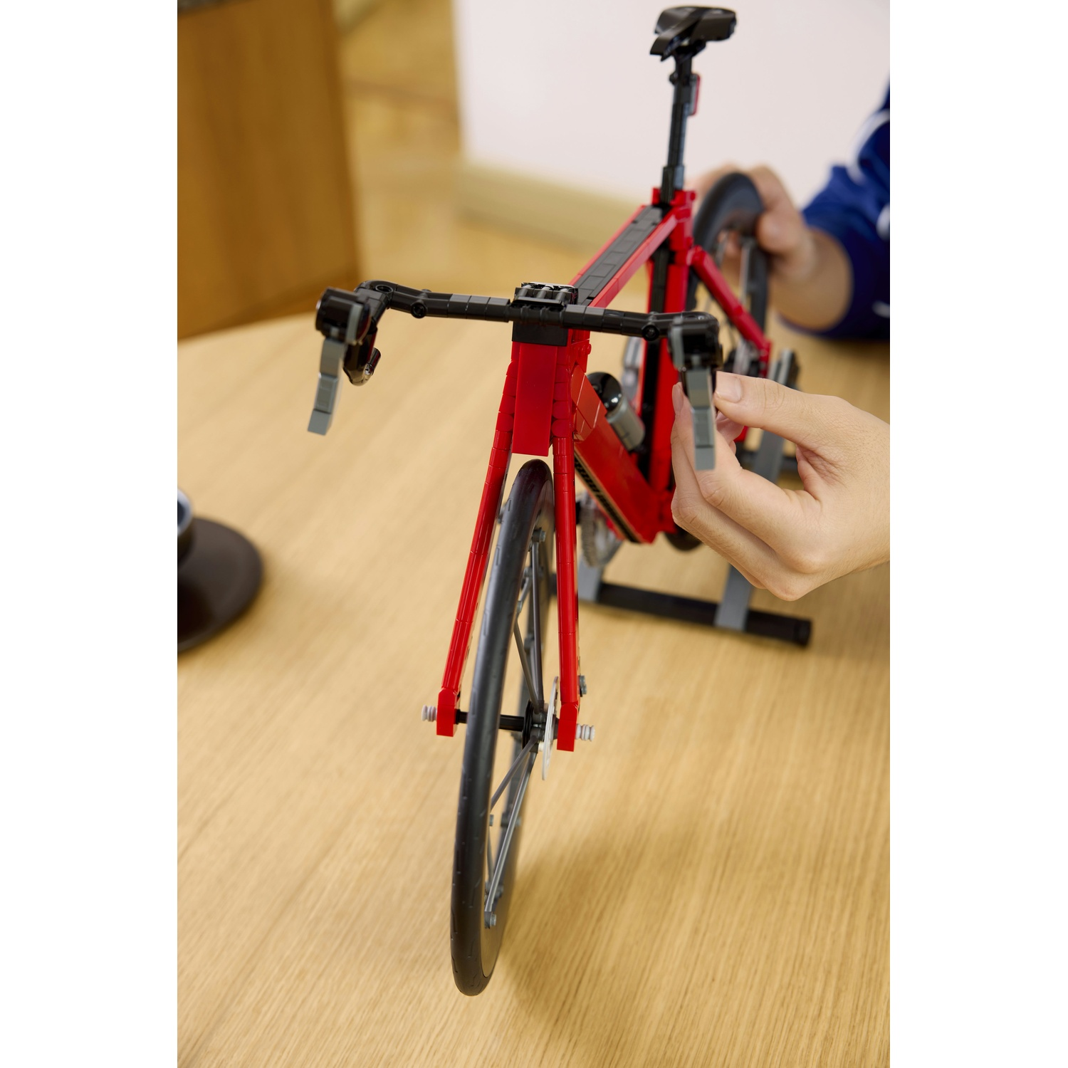 Un modello di bici da corsa rossa Lego su tavolo di legno. Mani interagiscono con esso.