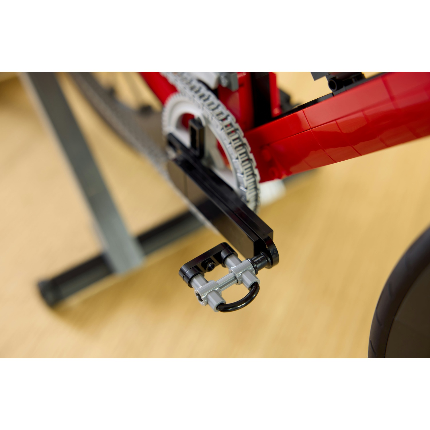 Primo piano di pedale e catena di una bicicletta Lego rossa su legno.