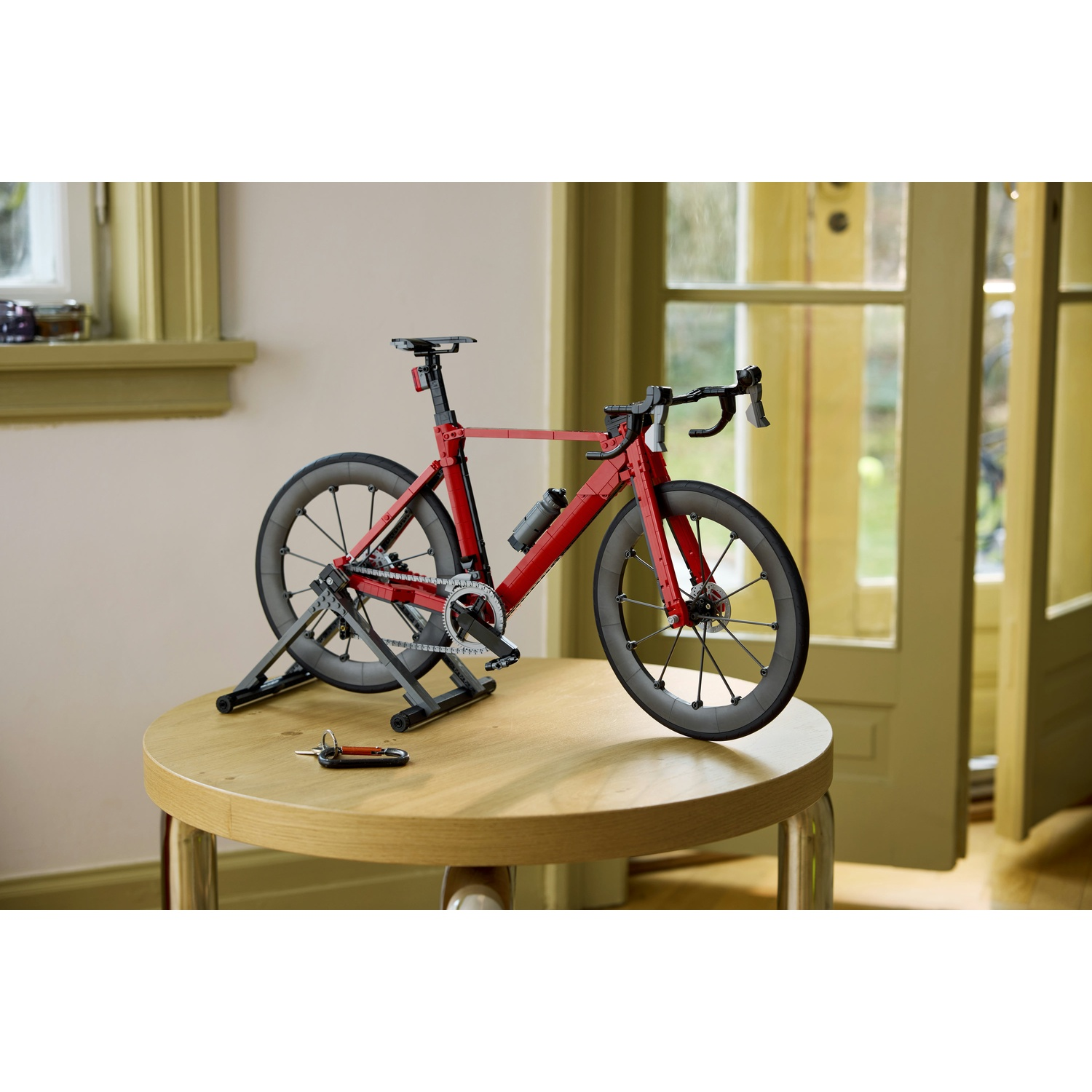 Una bicicletta Lego rossa su un supporto si trova su un tavolo di legno. Una borraccia è attaccata.