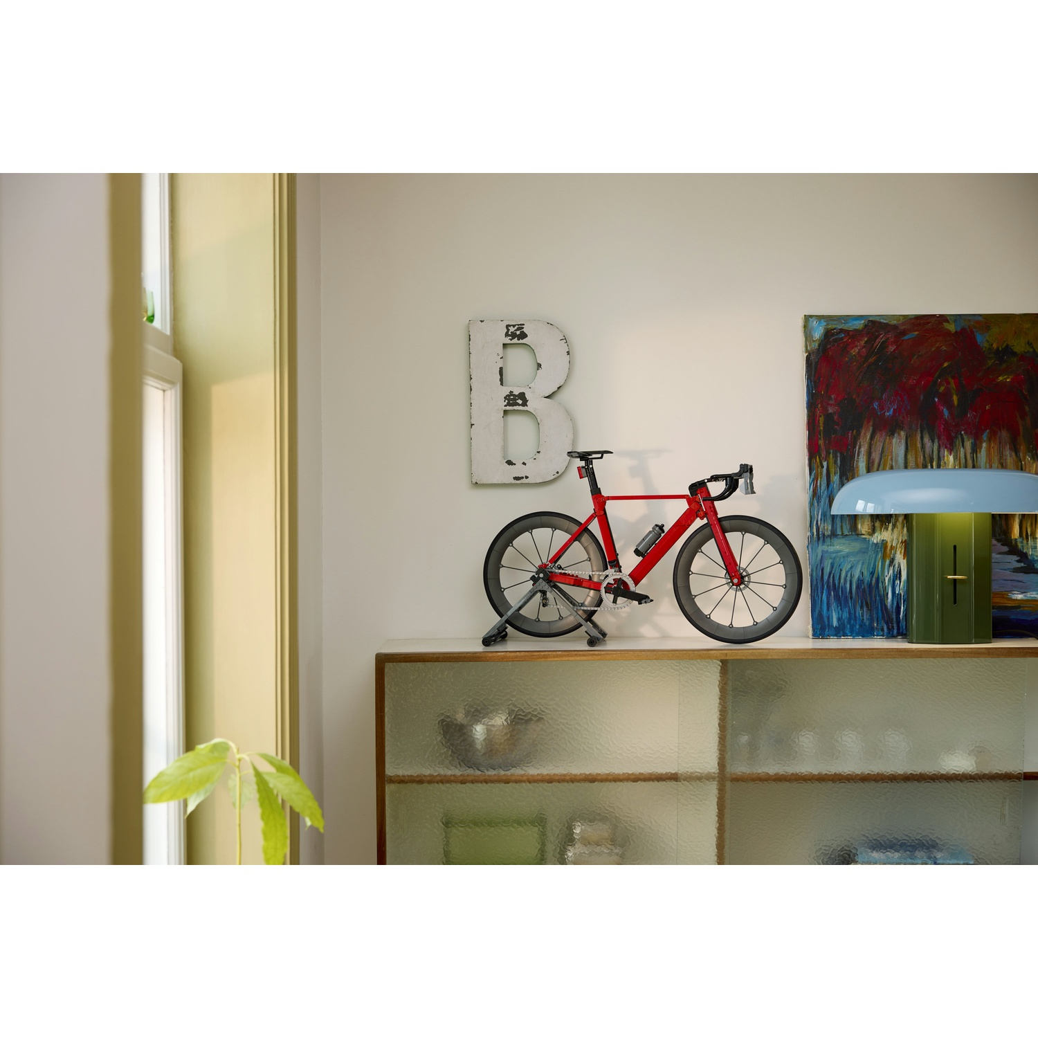 Una bicicletta da corsa rossa si trova su uno scaffale accanto a un quadro e una lampada.