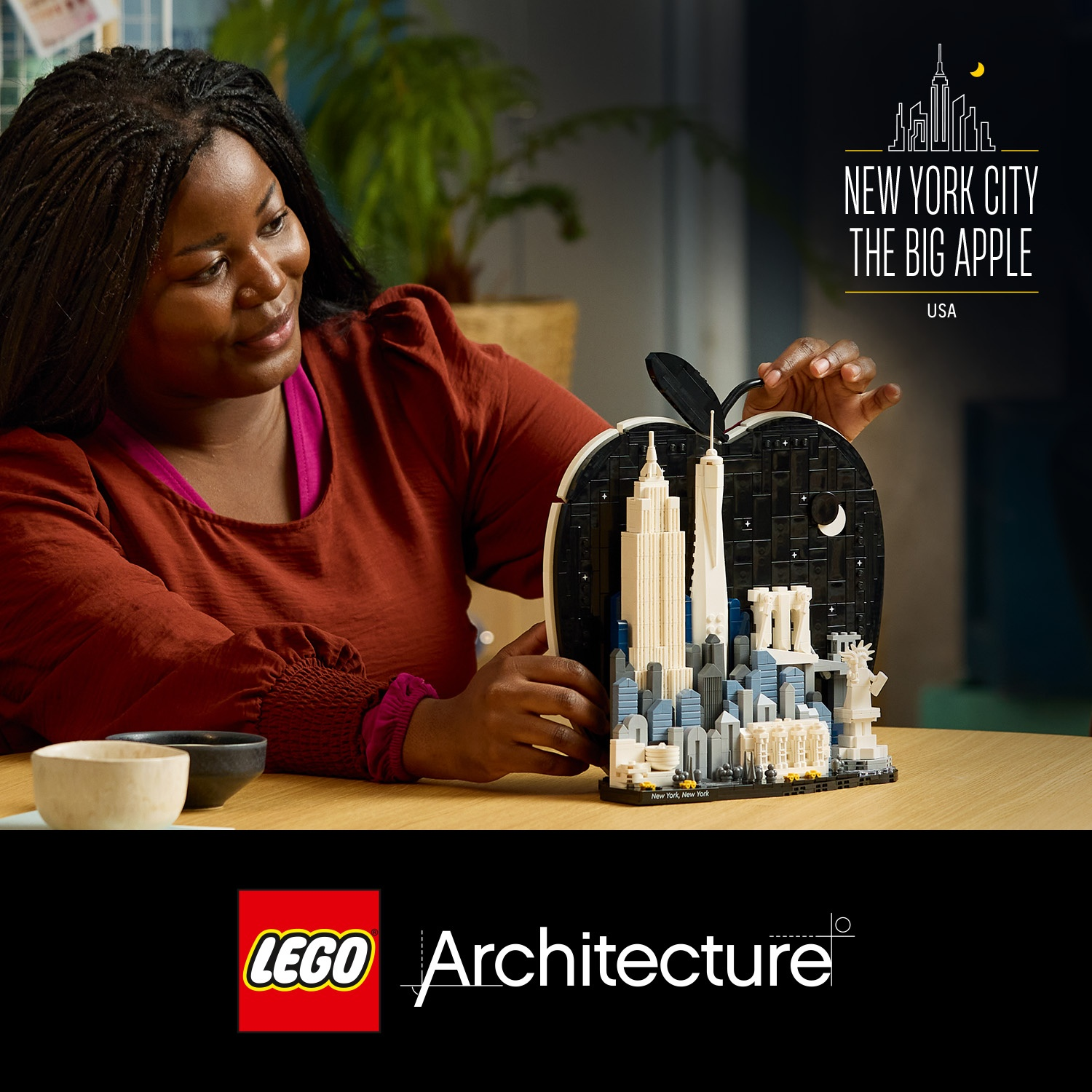 Donna con capelli intrecciati presenta un modello Lego di New York a forma di mela.