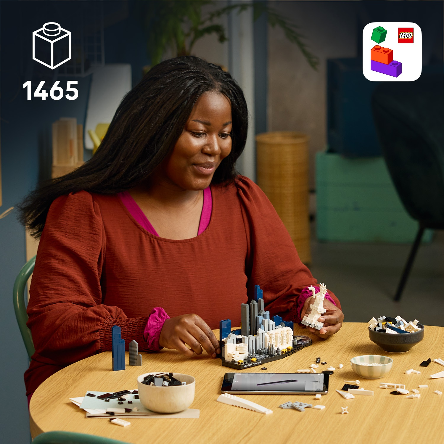Donna costruisce un modello Lego. Si vedono piccoli mattoncini Lego e istruzioni sul telefono.