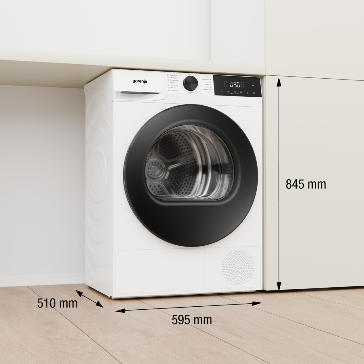 Ein weißer Gorenje-Wäschetrockner steht auf einem Holzboden unter einem Regal. Maße sind angegeben.