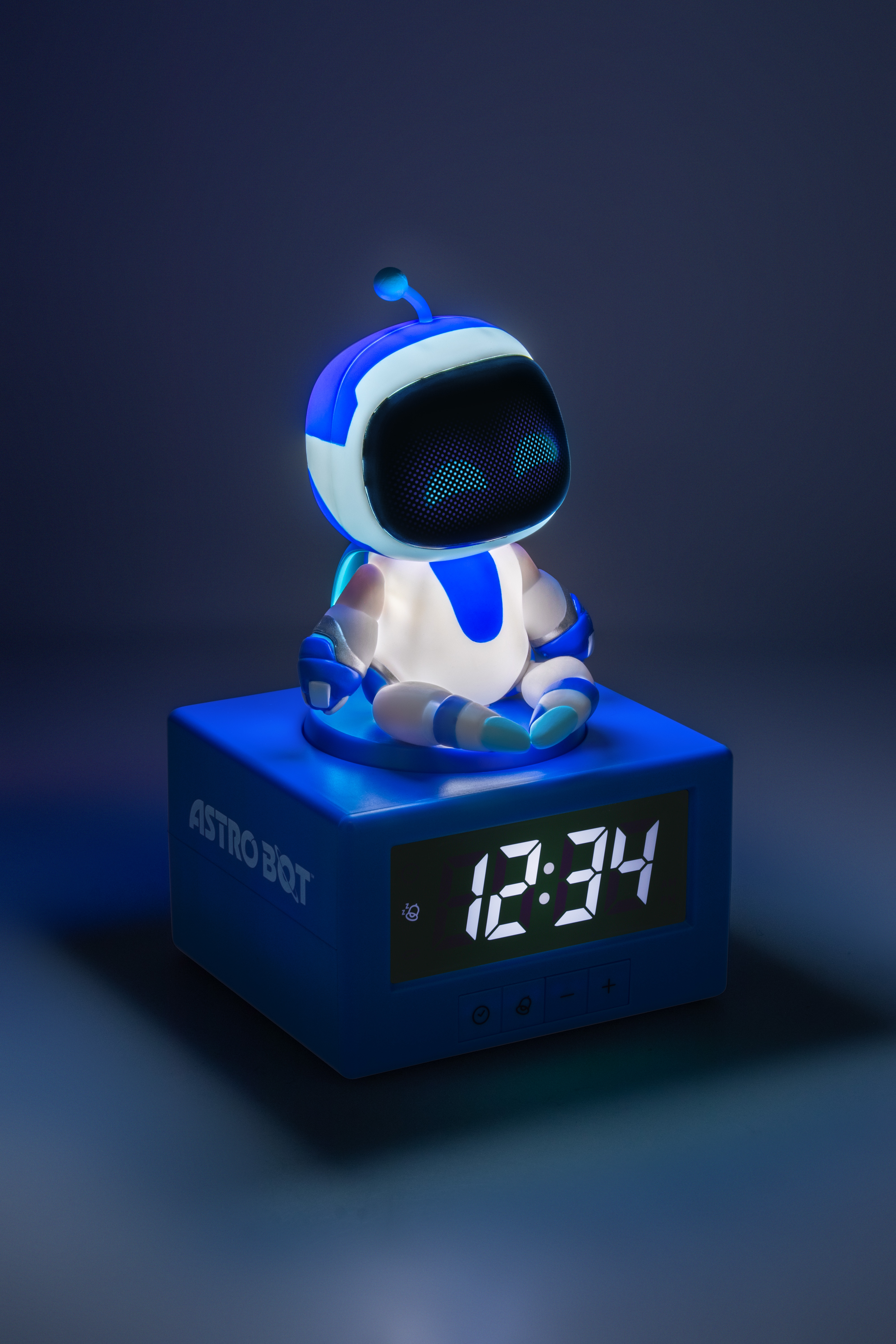 Ein blauer Astro Bot sitzt auf einem Würfel-Wecker mit der Zeit 12:34.
