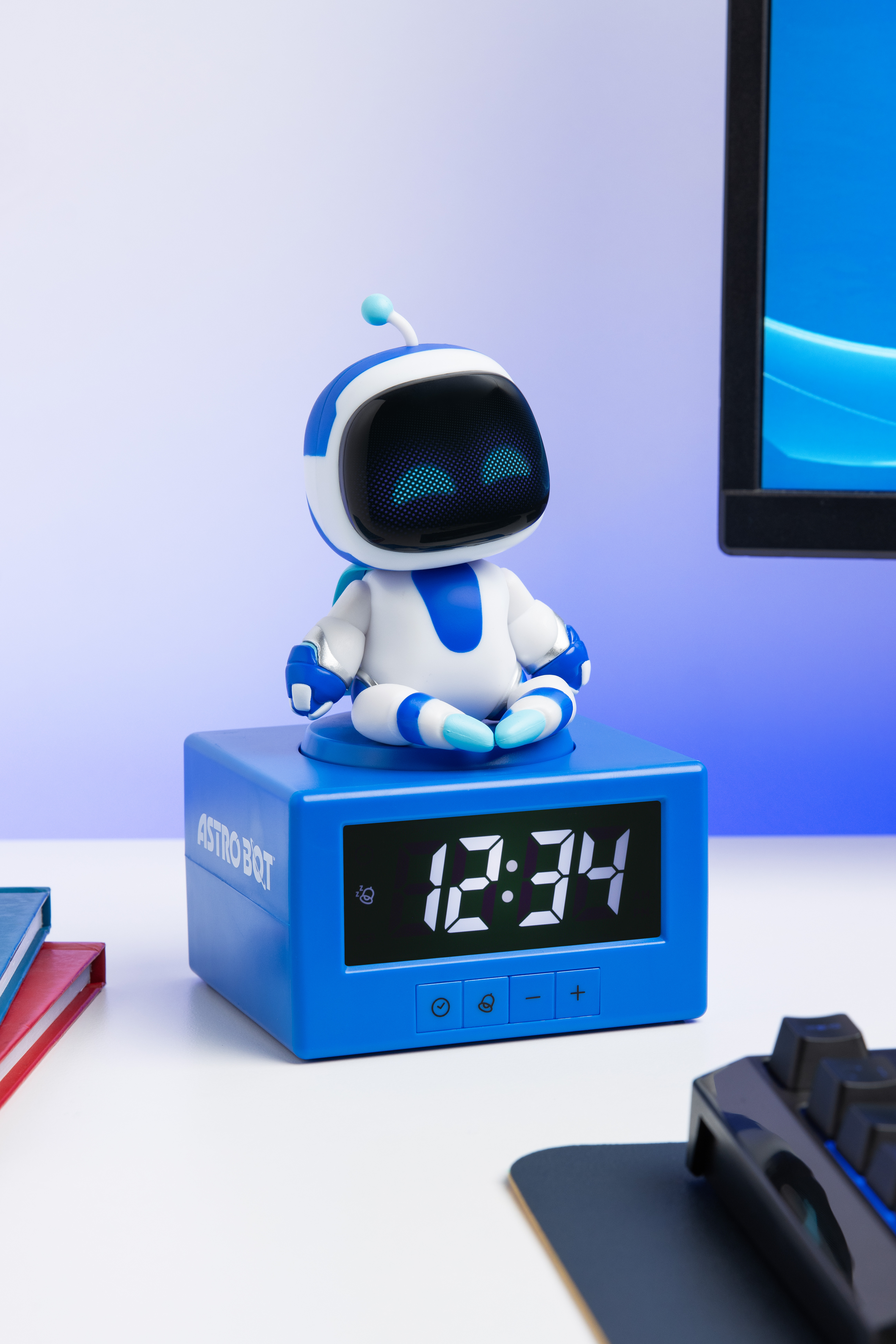 Astro Bot sitzt auf einem blauen Wecker mit der Zeit 12:34. Rechts ist ein Bildschirm.