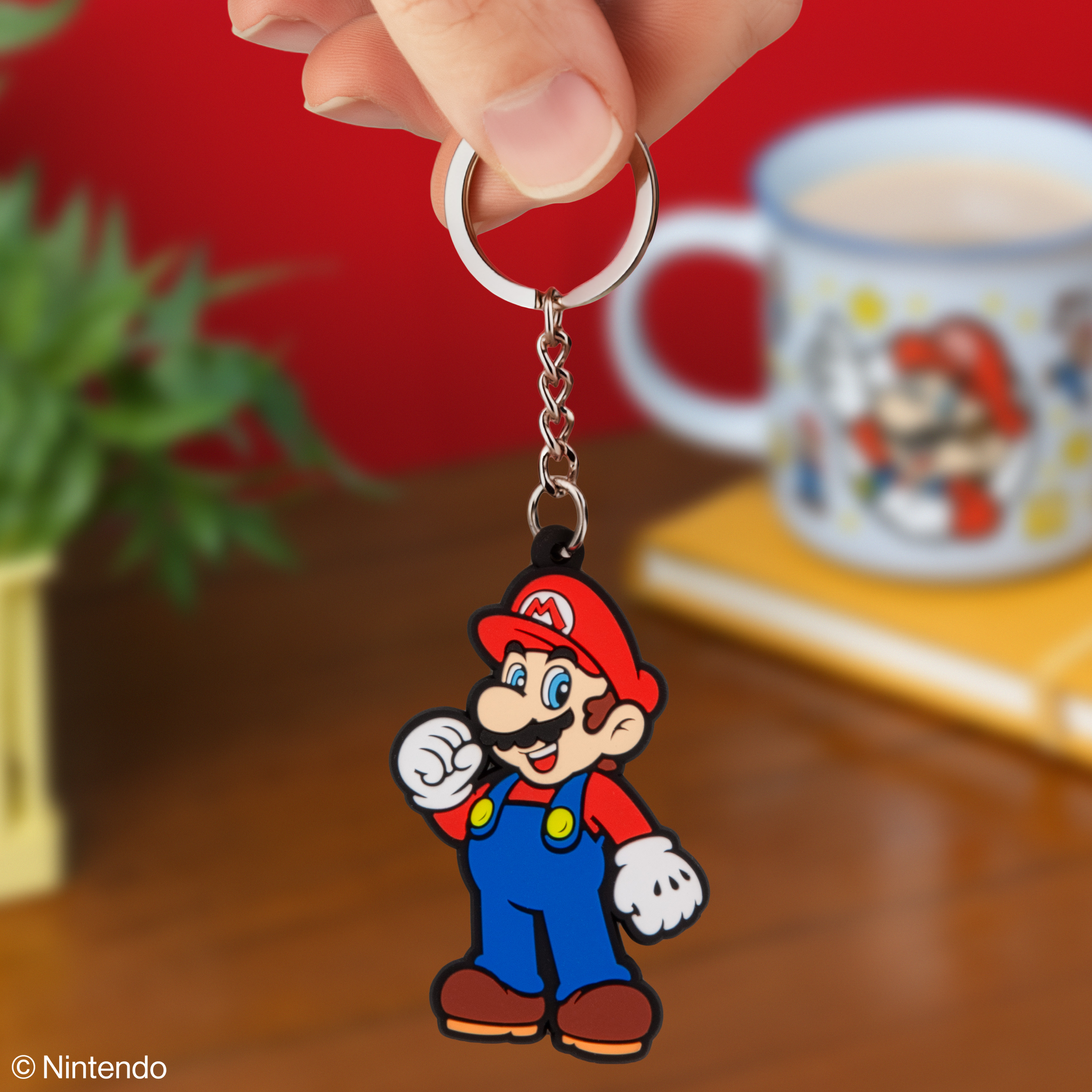 Ein Mario-Schlüsselanhänger in Rot, Blau und Gelb wird von Fingern gehalten.