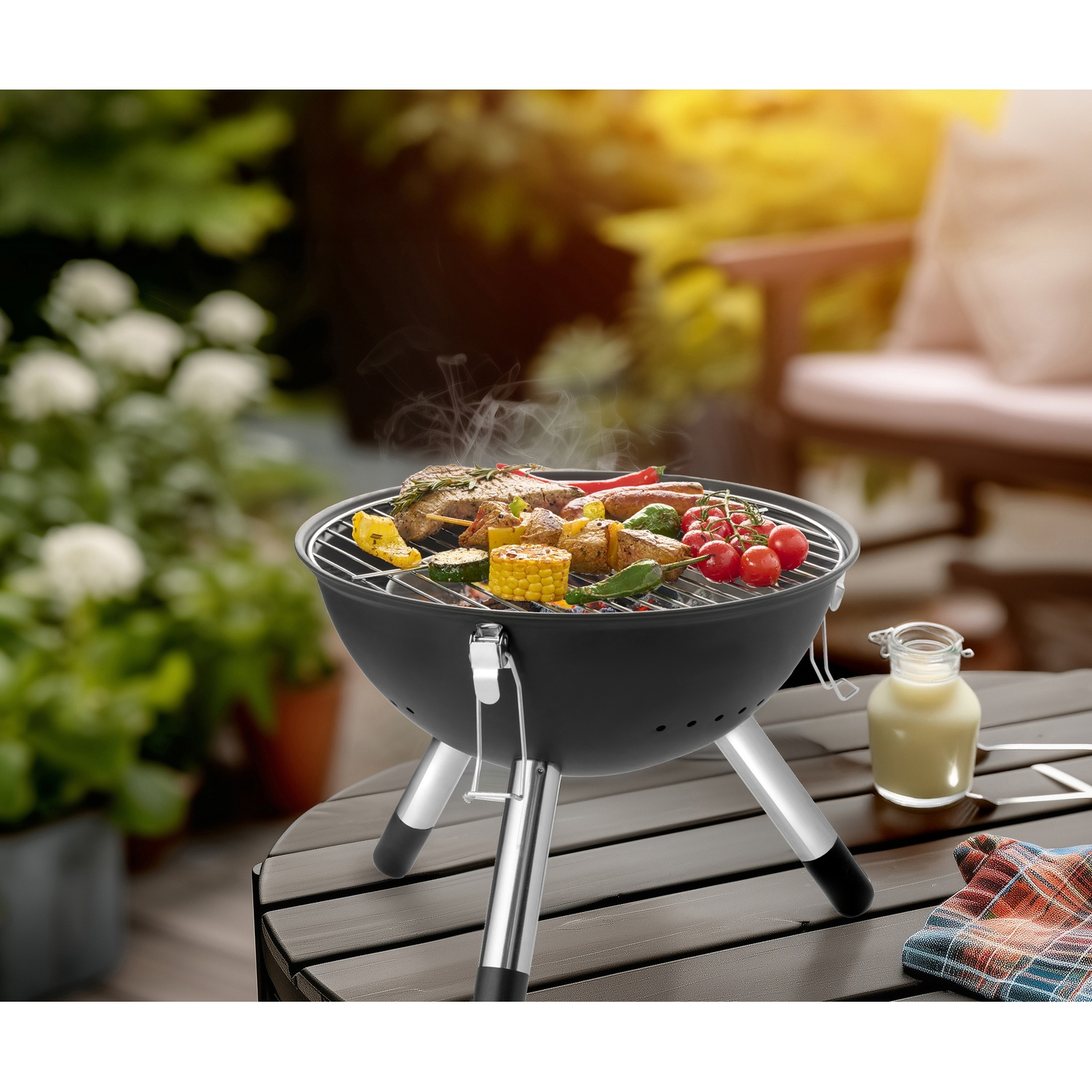 A black charcoal grill with food cooking on it sits on a wooden table.