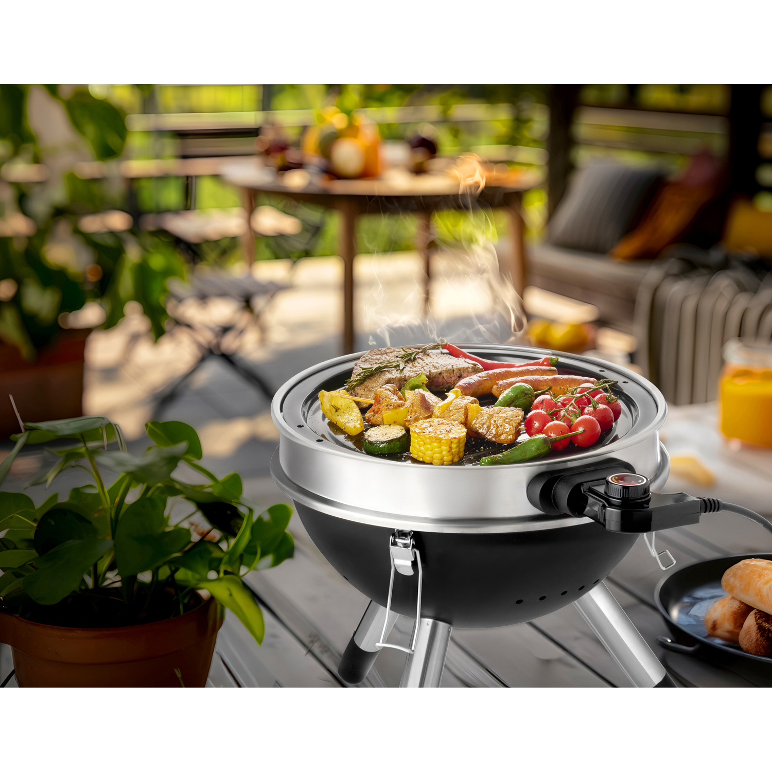 Electric grill with meat, sausages, vegetables, and tomatoes on a patio.
