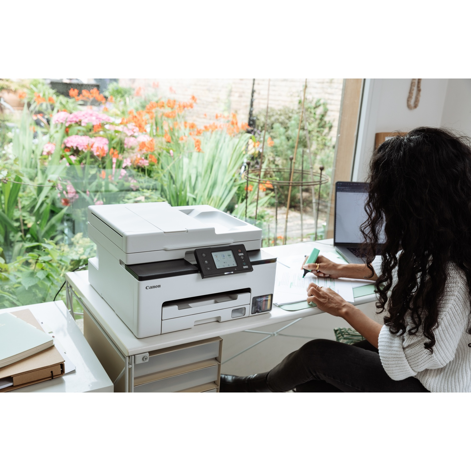 Een vrouw zit aan een bureau, werkend aan documenten naast een printer.