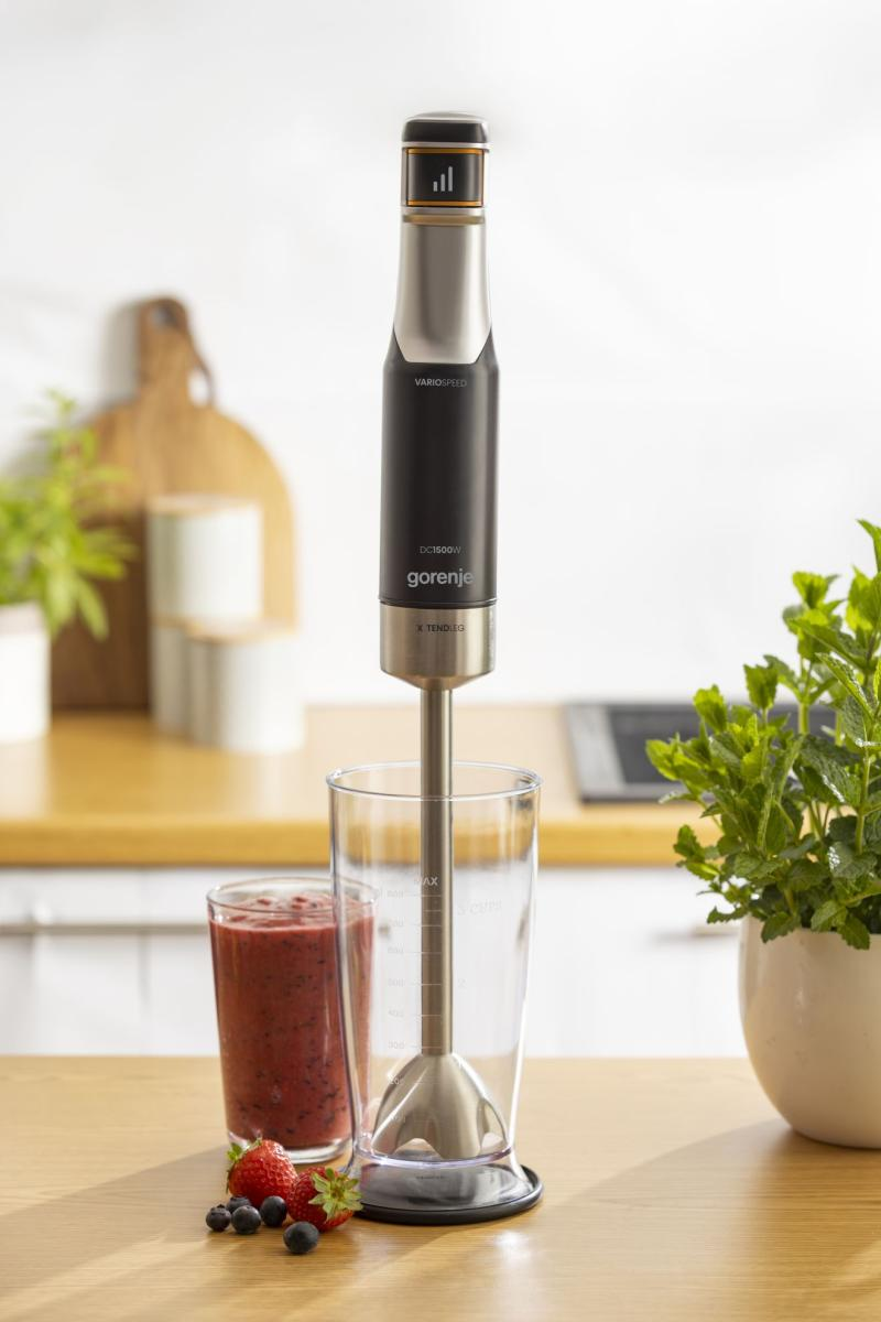 Blender ręczny z koktajlem jagodowym, jagodami i miętą na drewnianym stole.
