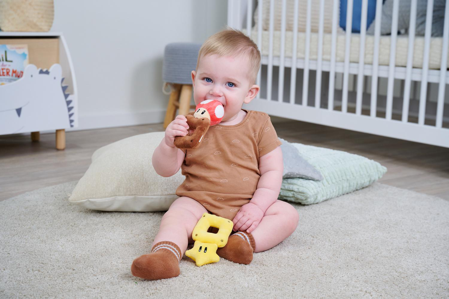Ein Baby sitzt auf einem Teppich und spielt mit einem Pilz-Beißring und einem gelben Sternspielzeug.