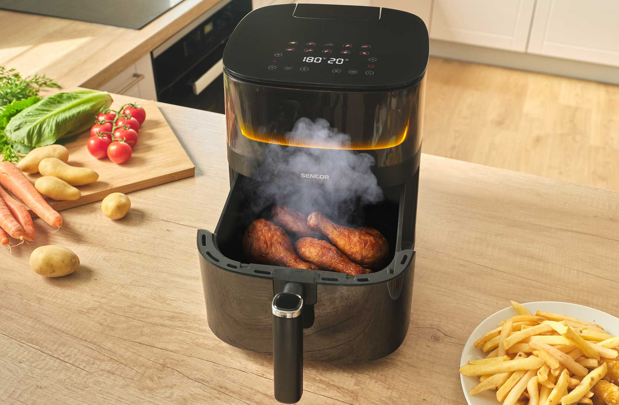 Fekete légkeveréses fritőz csirkecombokkal és gőzzel. Mellette sült krumpli van.