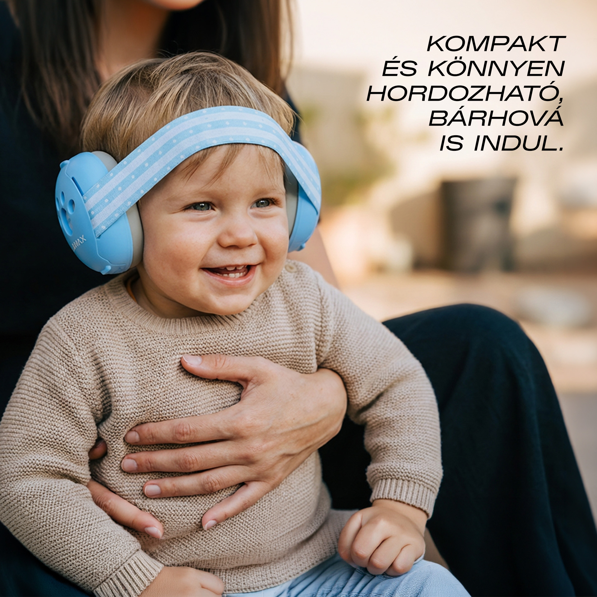 Mosolygó kisgyerek kék fülvédőben, egy felnőtt tartja.