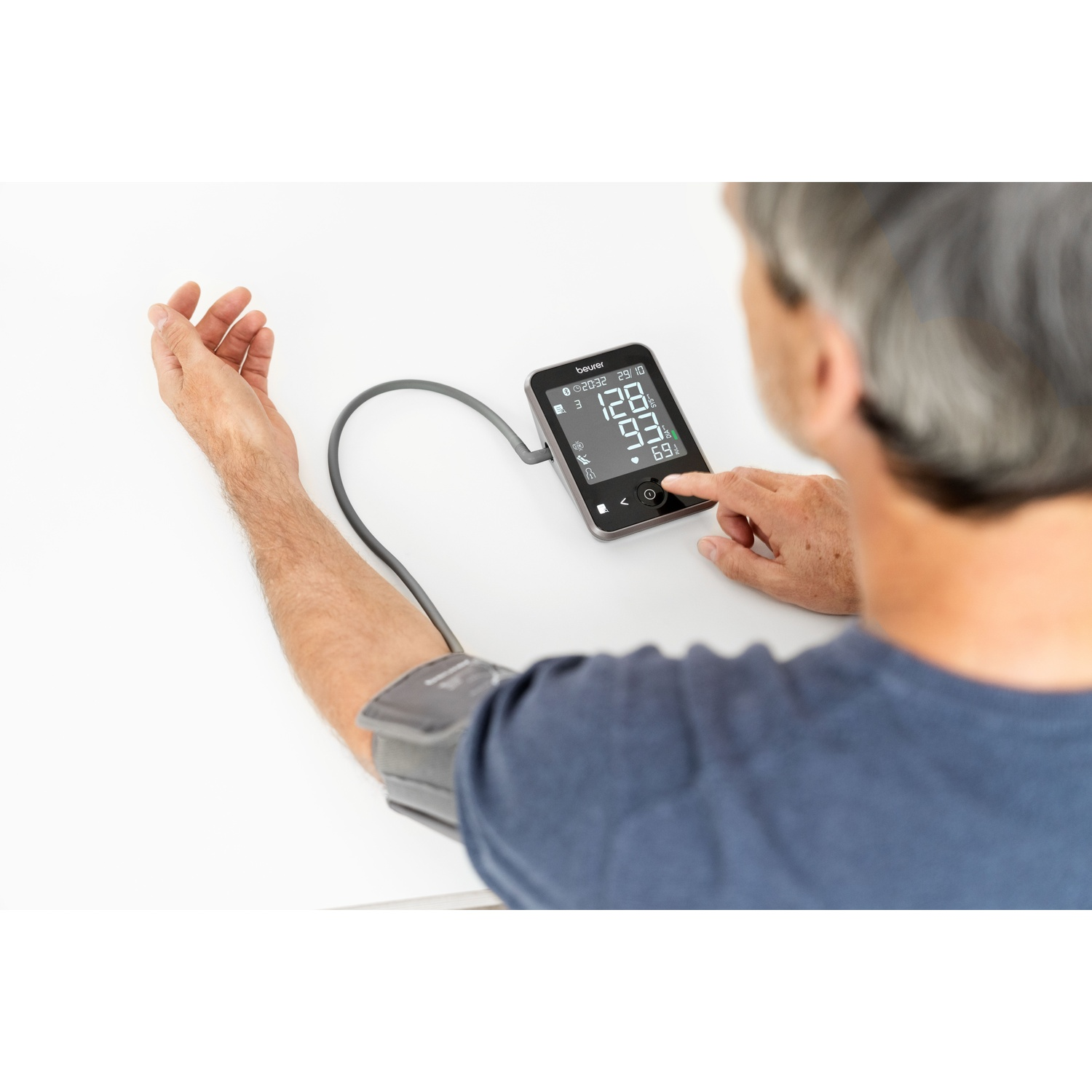 Man using a blood pressure monitor on his arm. Display shows numbers.
