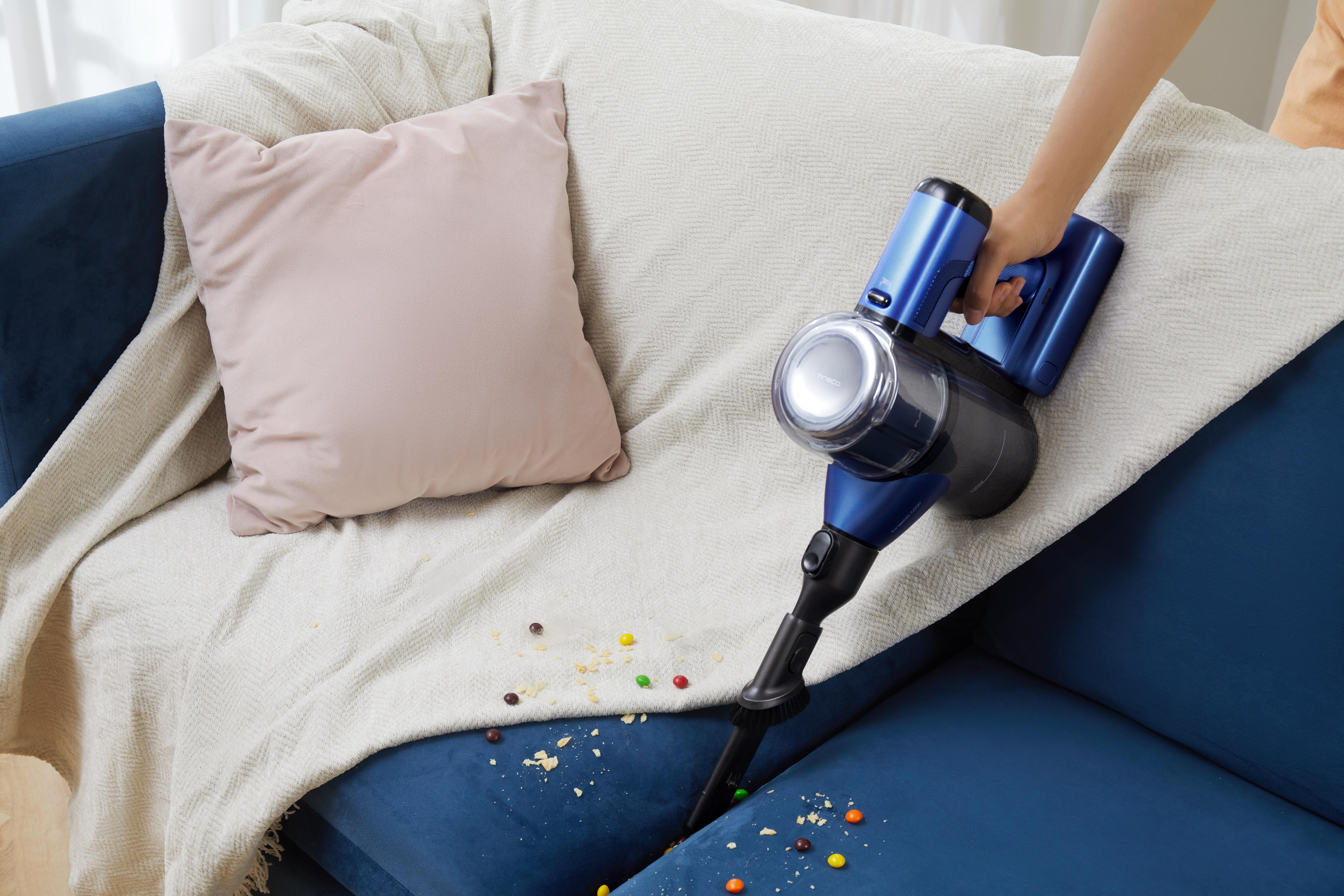 Blaue Handstaubsauger reinigt Couch von Süßigkeiten und Krümeln.