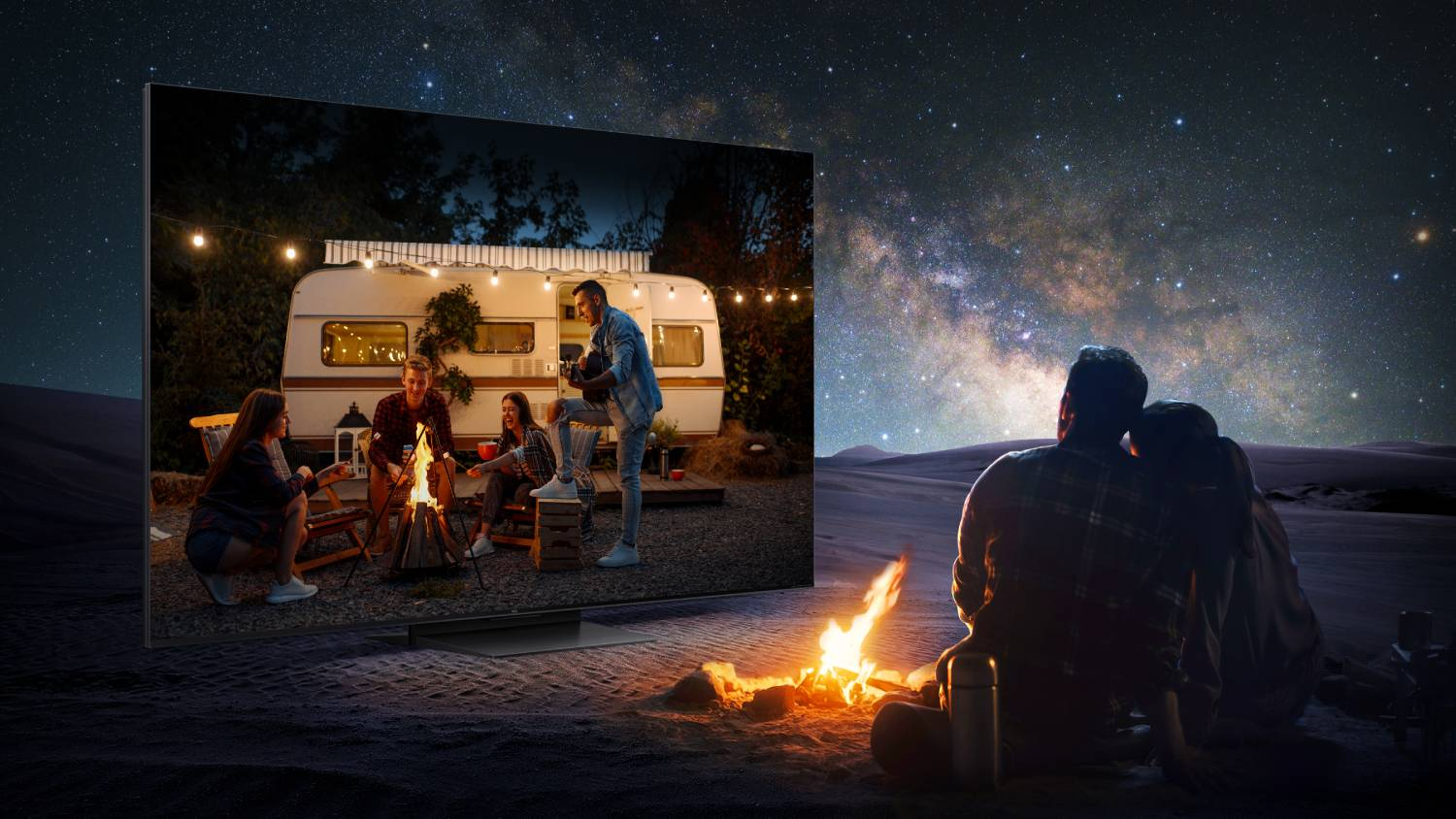 Amigos acampan junto a una fogata frente a una caravana bajo un cielo estrellado.