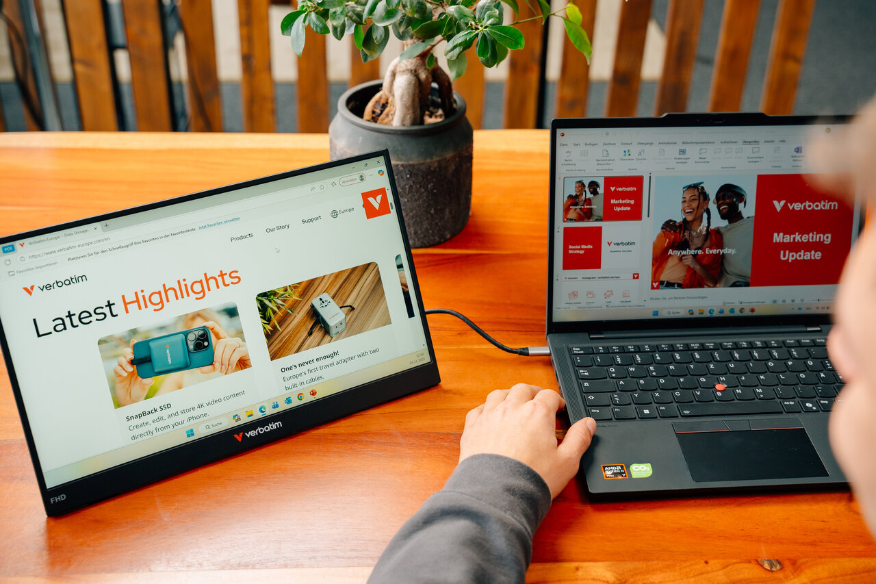 Un laptop e un monitor esterno mostrano contenuti del sito Verbatim su un tavolo di legno.