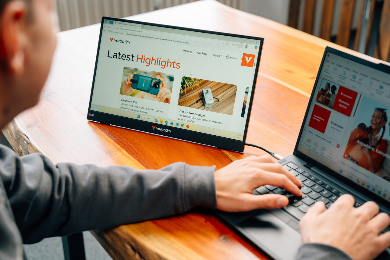 Persona digita su laptop, monitor esterno mostra sito Verbatim con highlights.