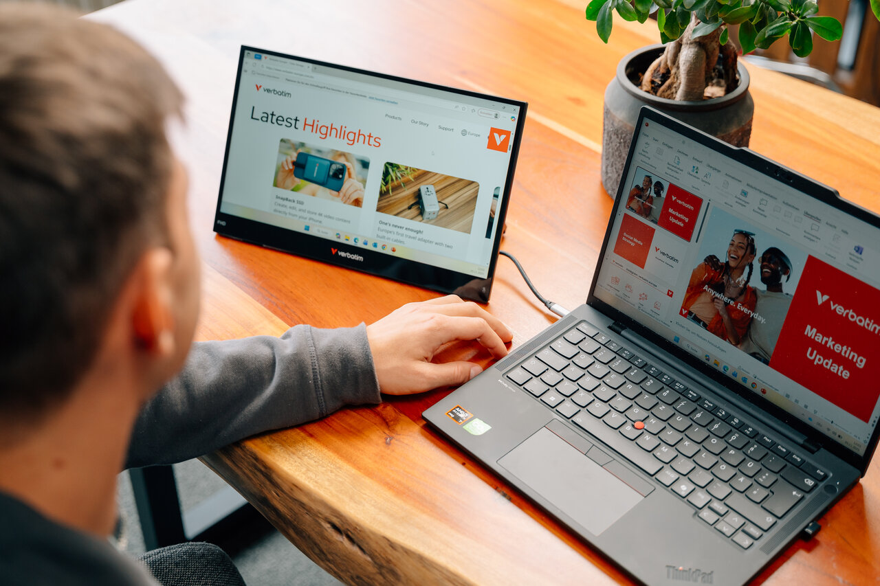 Una persona lavora su un laptop e un monitor esterno su una scrivania di legno.