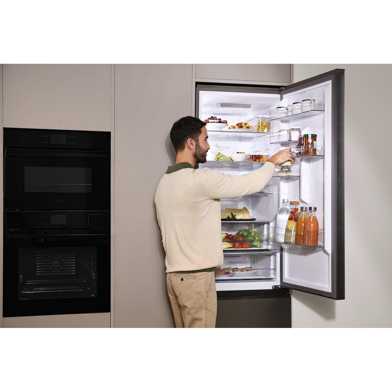 Uomo chiude porta frigo in cucina. Forni visibili a sinistra.