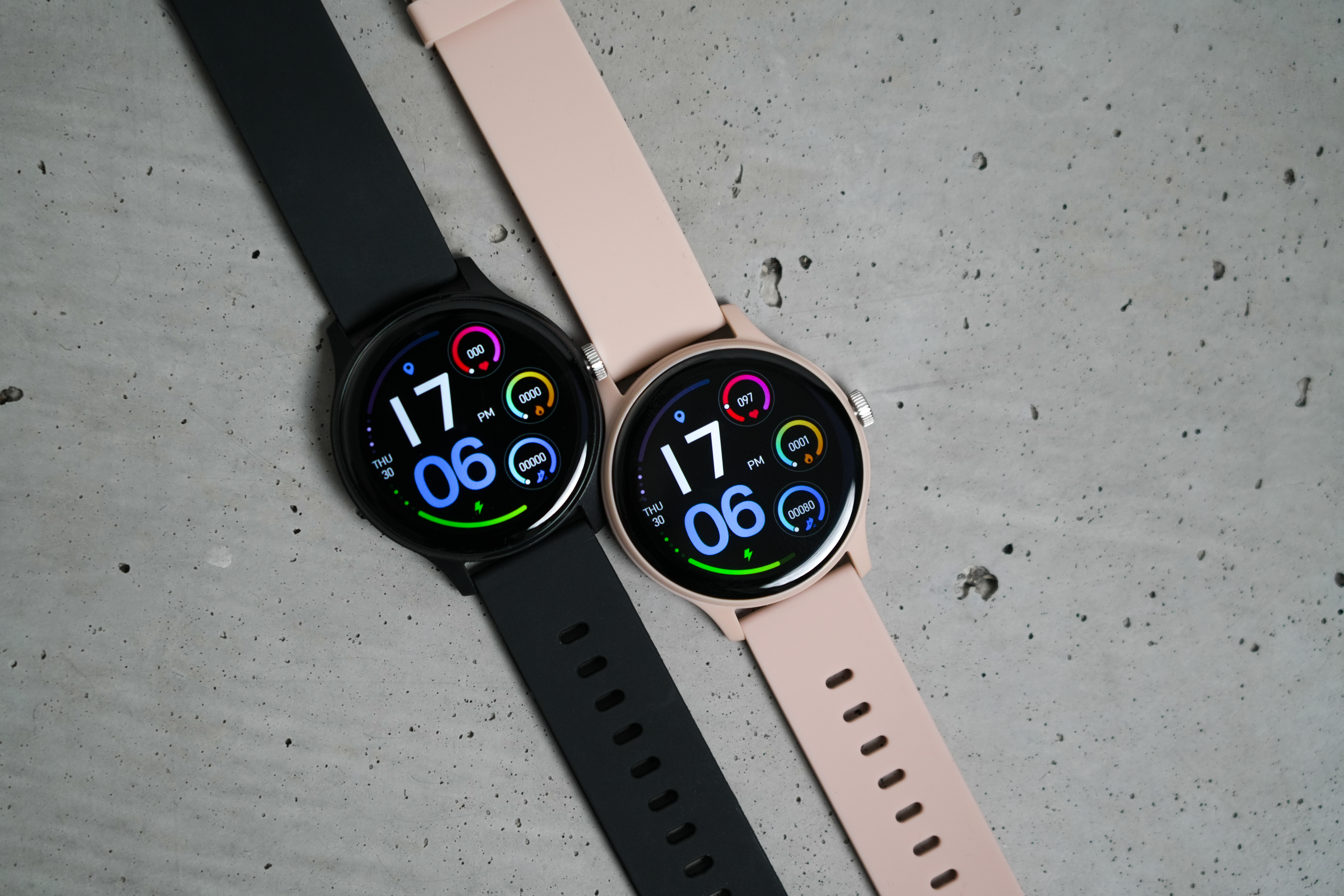 Due smartwatch, una nera, una rosa pallido, su cemento.