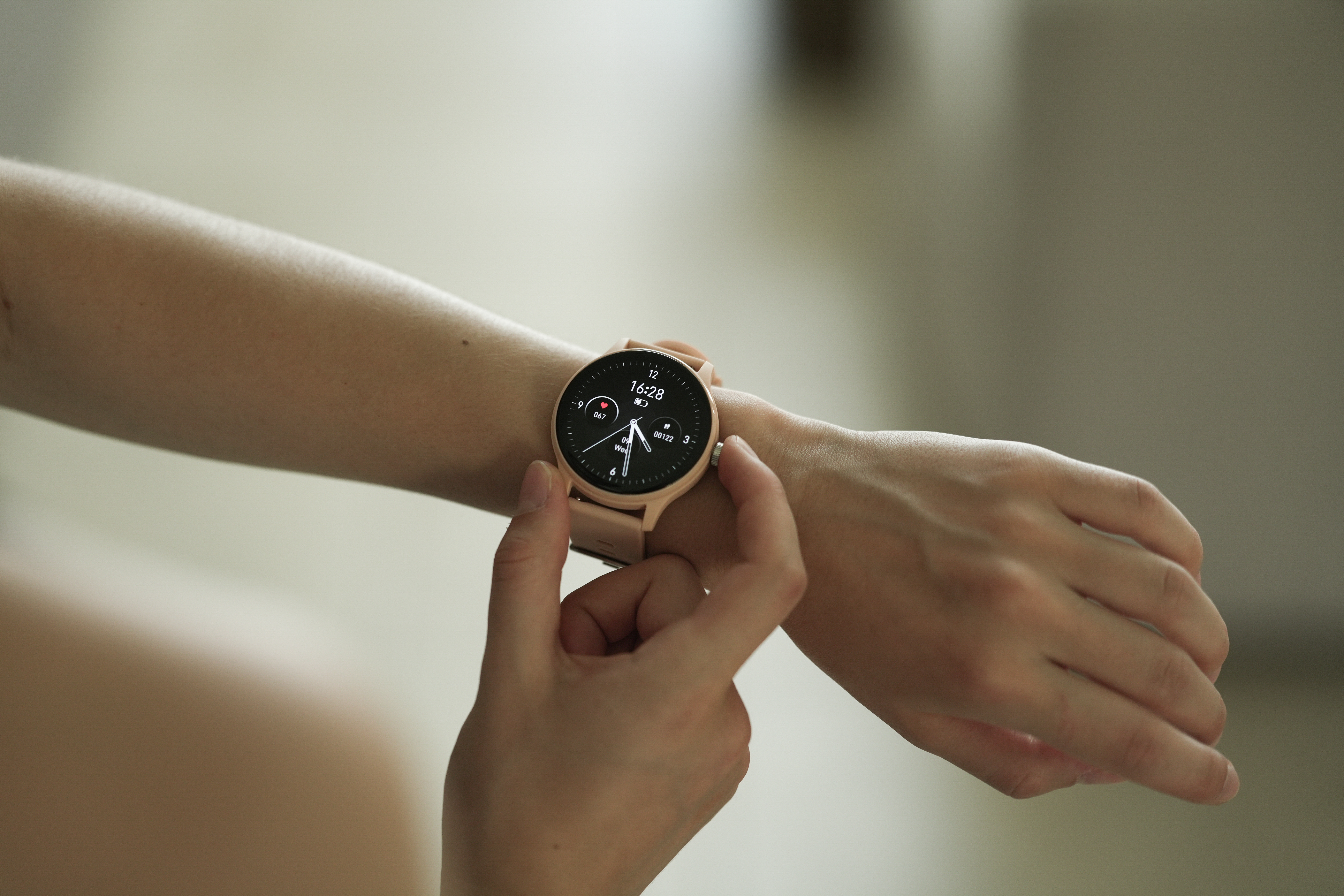 Una persona indossa uno smartwatch rosa al polso. L'orologio mostra le 16:28.
