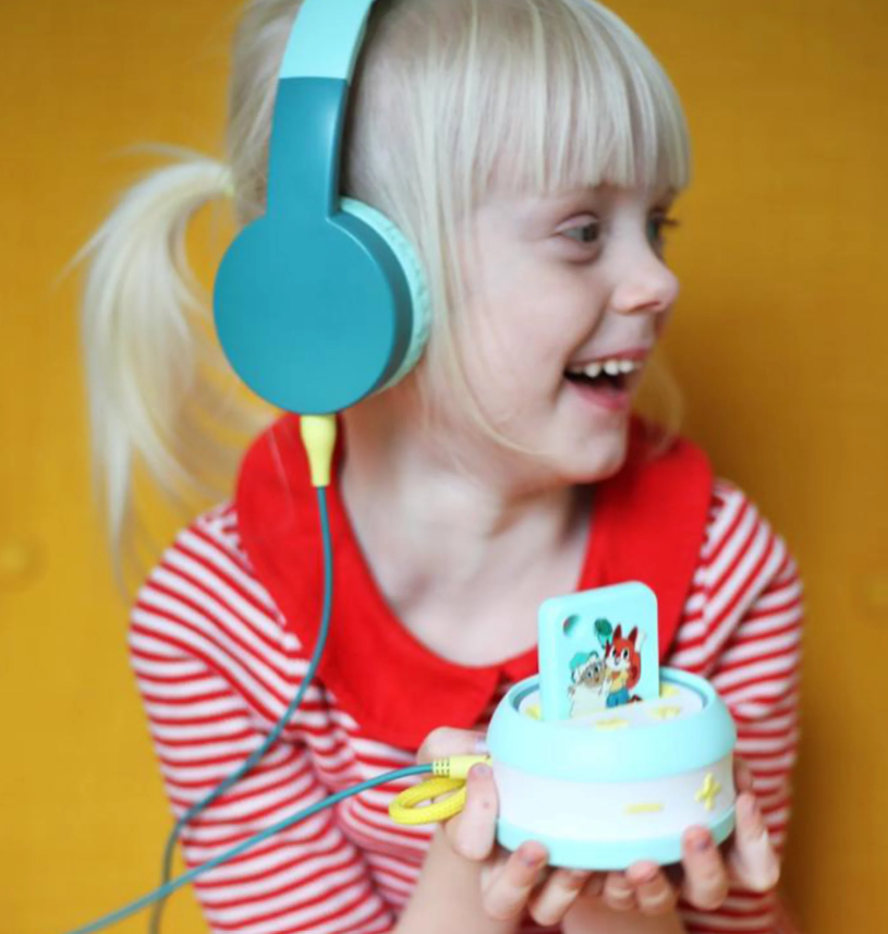 Ein Mädchen mit Kopfhörern hält ein Spielzeug, das wie ein kleiner Lautsprecher aussieht.