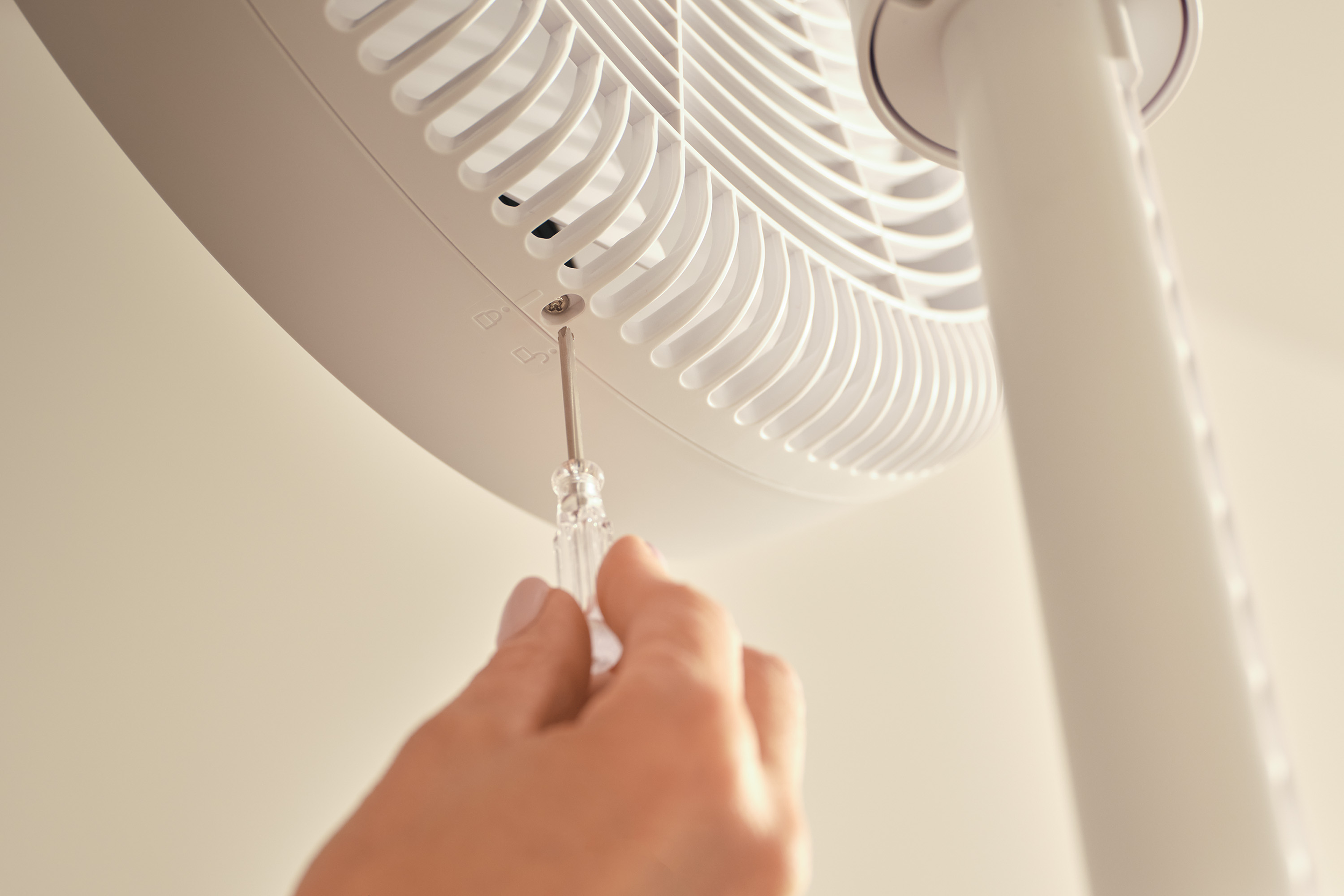 Egy kéz csavarhúzóval lazít egy csavart egy fehér ventilátoron.