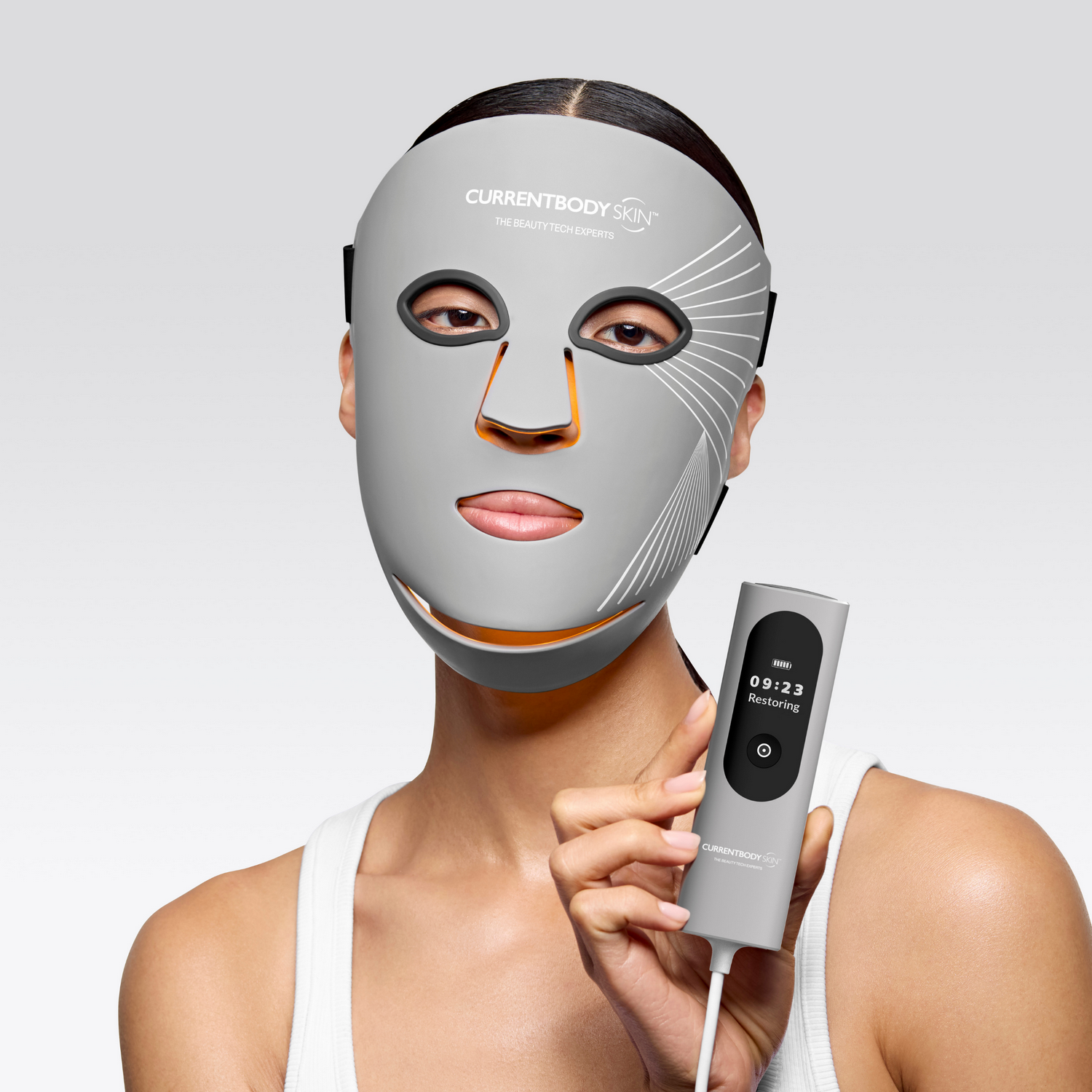Una mujer lleva una mascarilla facial LED gris y sostiene un dispositivo de control.