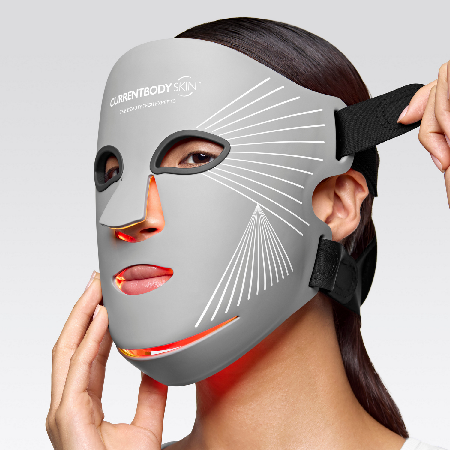 Una mujer usa una máscara facial LED gris con luces rojas que iluminan su nariz y labios.