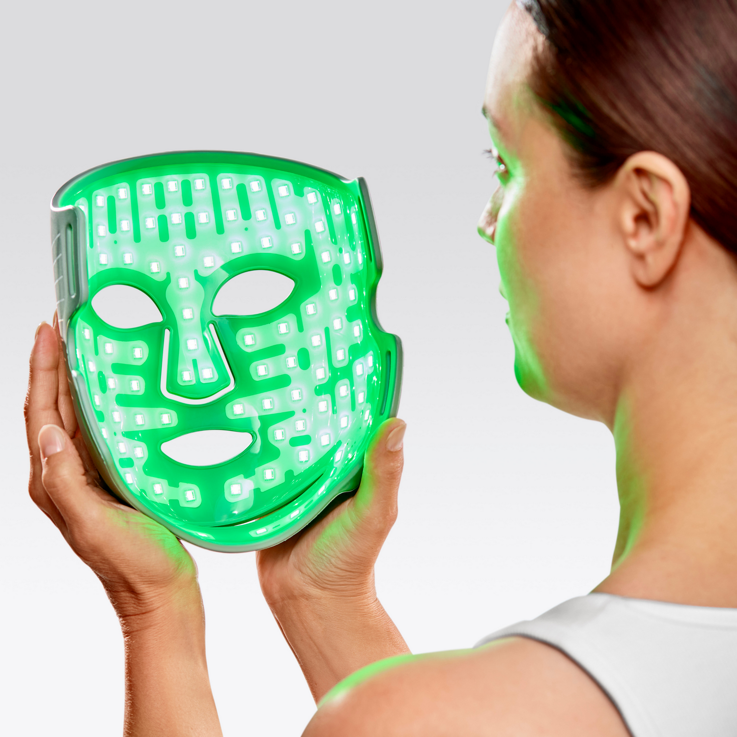 Mujer sostiene una máscara LED verde con luces delante de su cara.