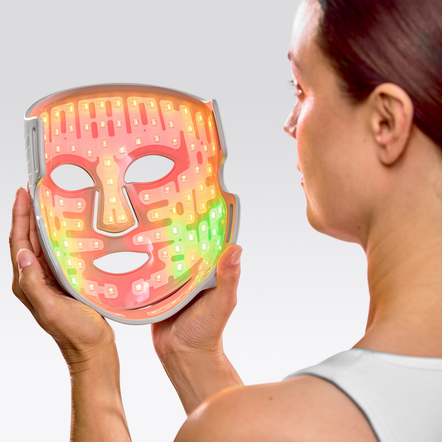 Una mujer sostiene una mascarilla facial LED multicolor. La mascarilla tiene luces rojas, naranjas, amarillas y verdes.