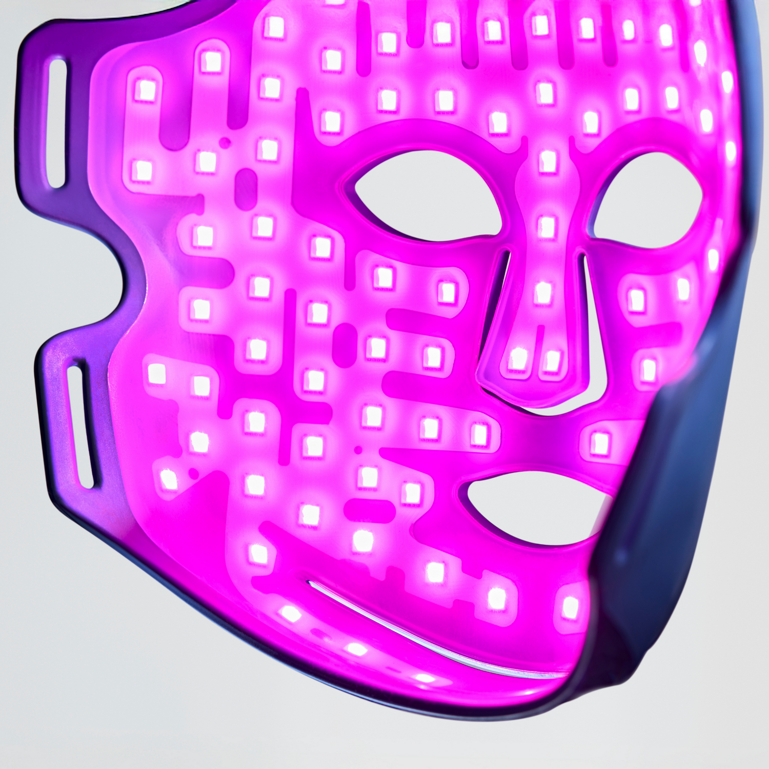 Una mascarilla facial LED morada con recortes para ojos y boca sobre fondo claro.