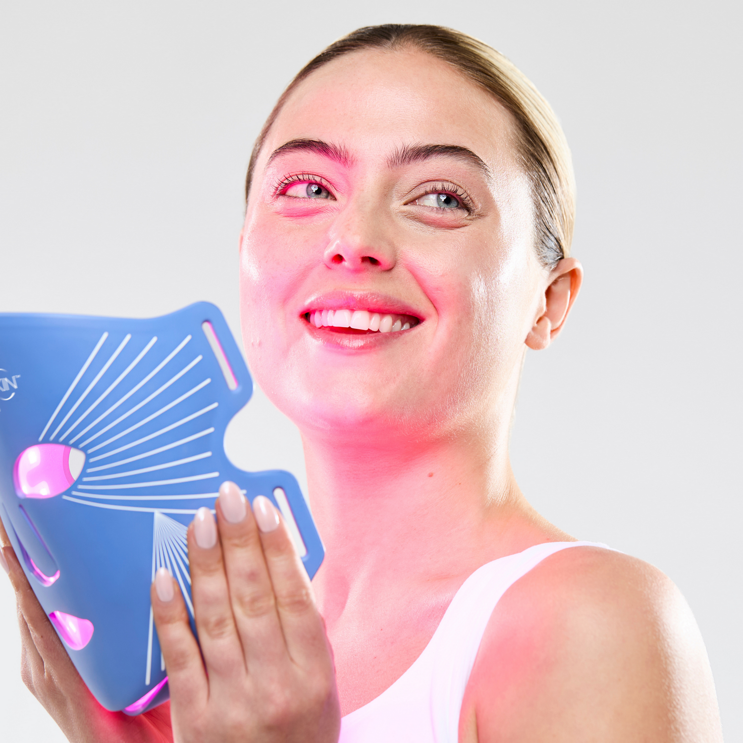 Mujer sosteniendo una mascarilla azul LED en su rostro, emitiendo luz roja.