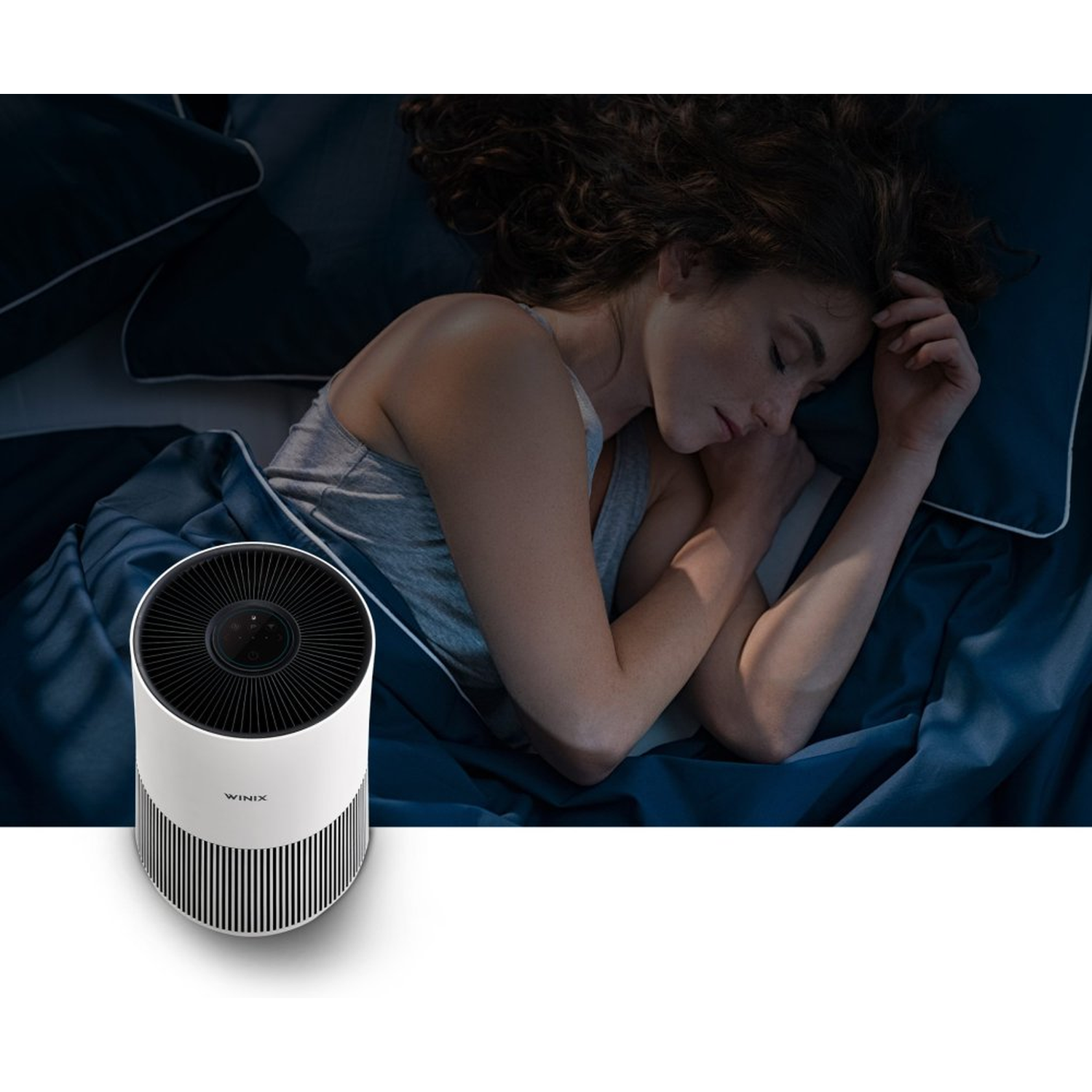 A woman sleeps in bed next to a white air purifier.