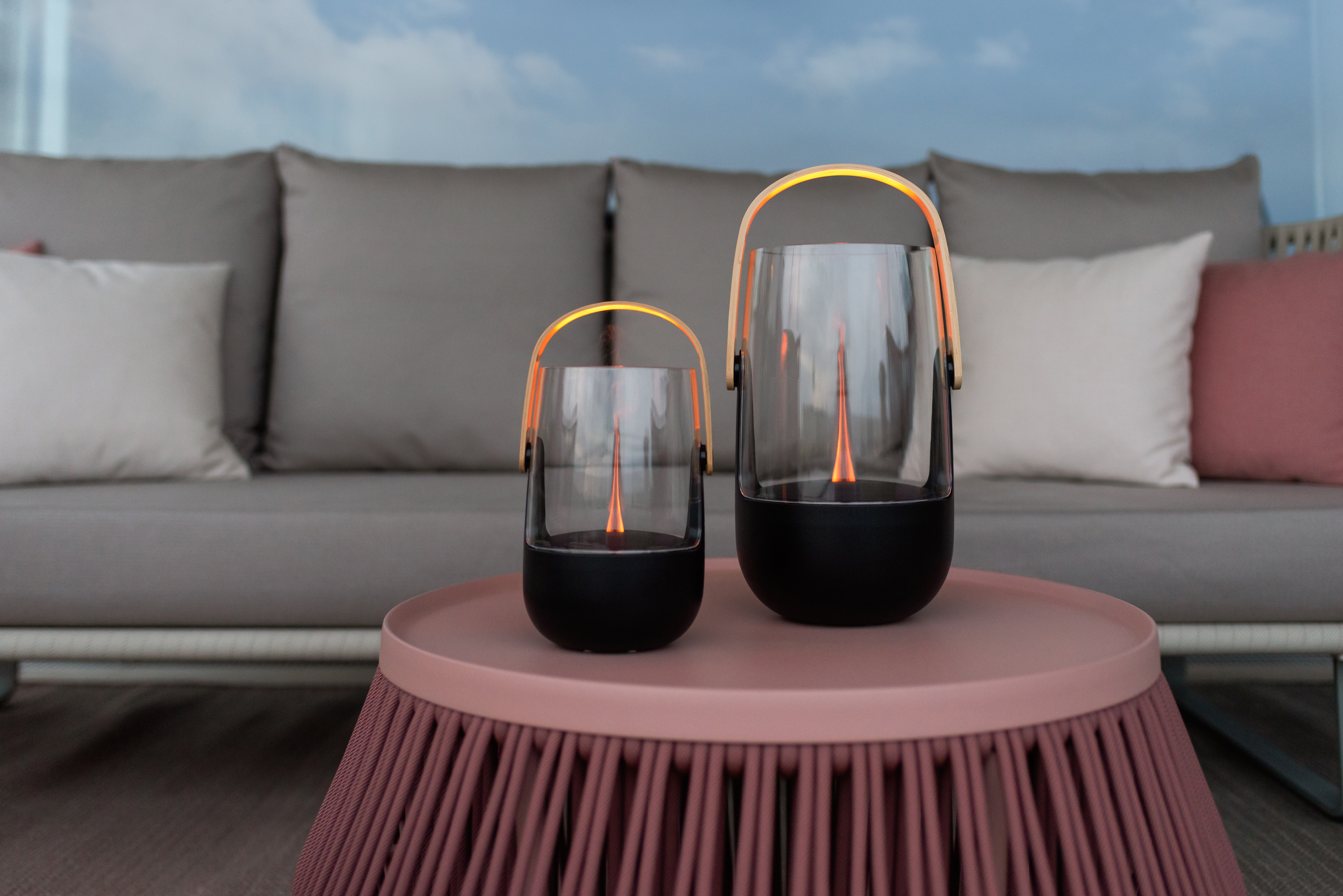 Zwei Glaslaternen mit Holzgriffen und Flammen stehen auf einem rosafarbenen Tisch.