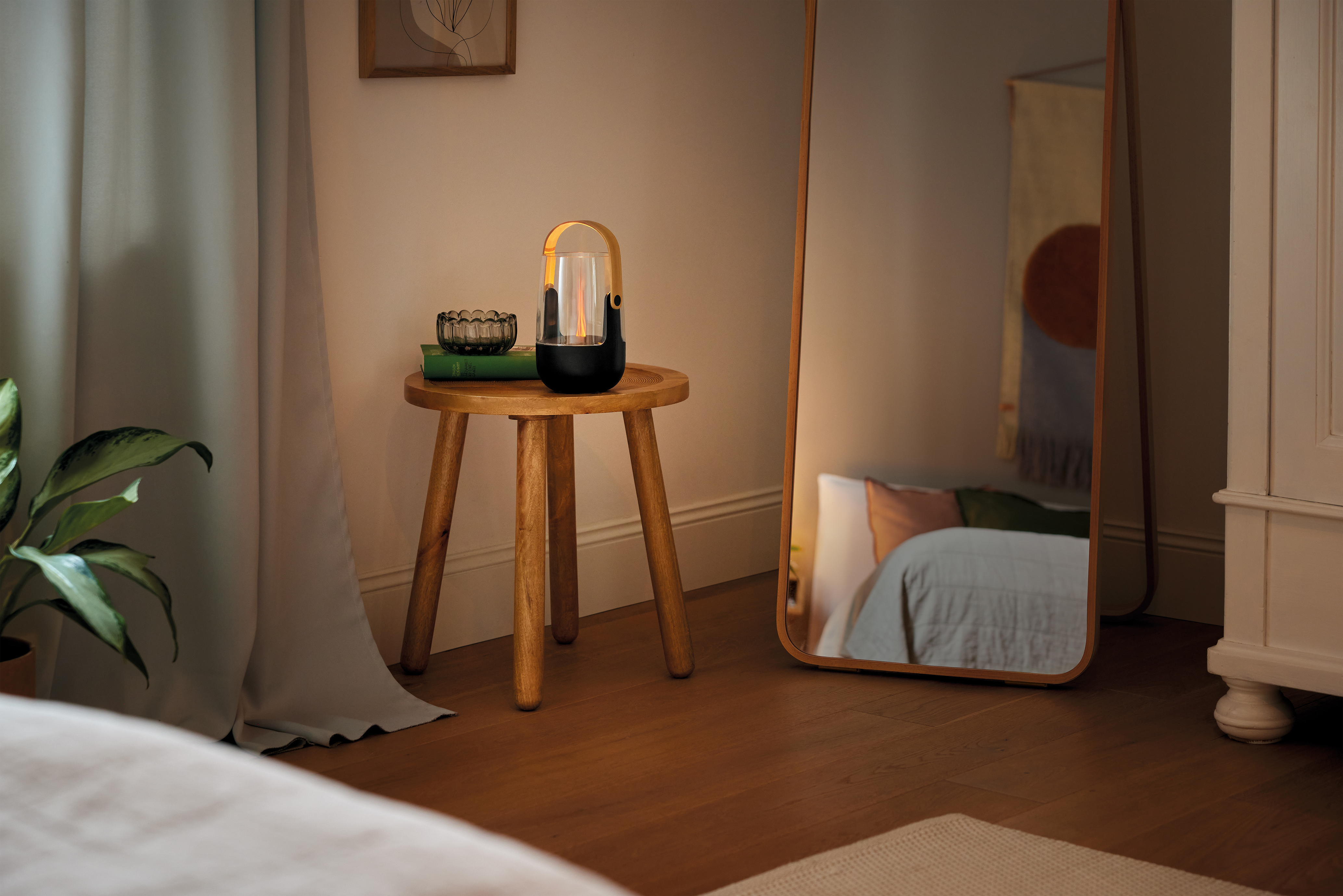 Ein Holzhocker mit Lampe, Buch und Glas auf einem Holzboden neben einem Spiegel.