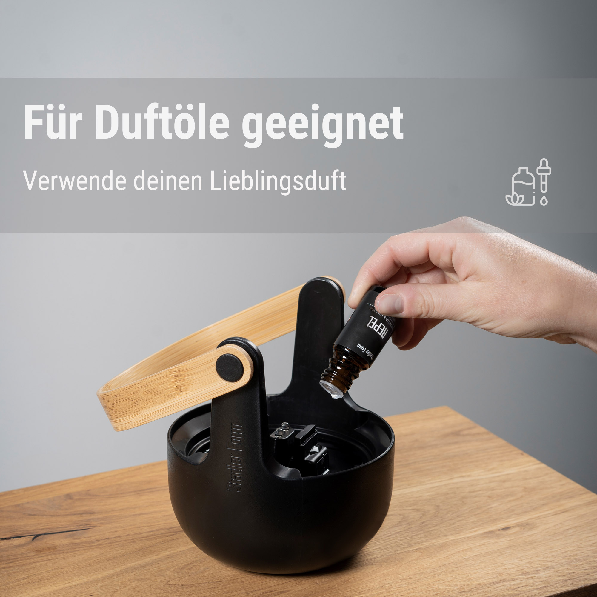 Eine Hand fügt Duftöl zu einem schwarzen Diffusor auf einem Holztisch hinzu.