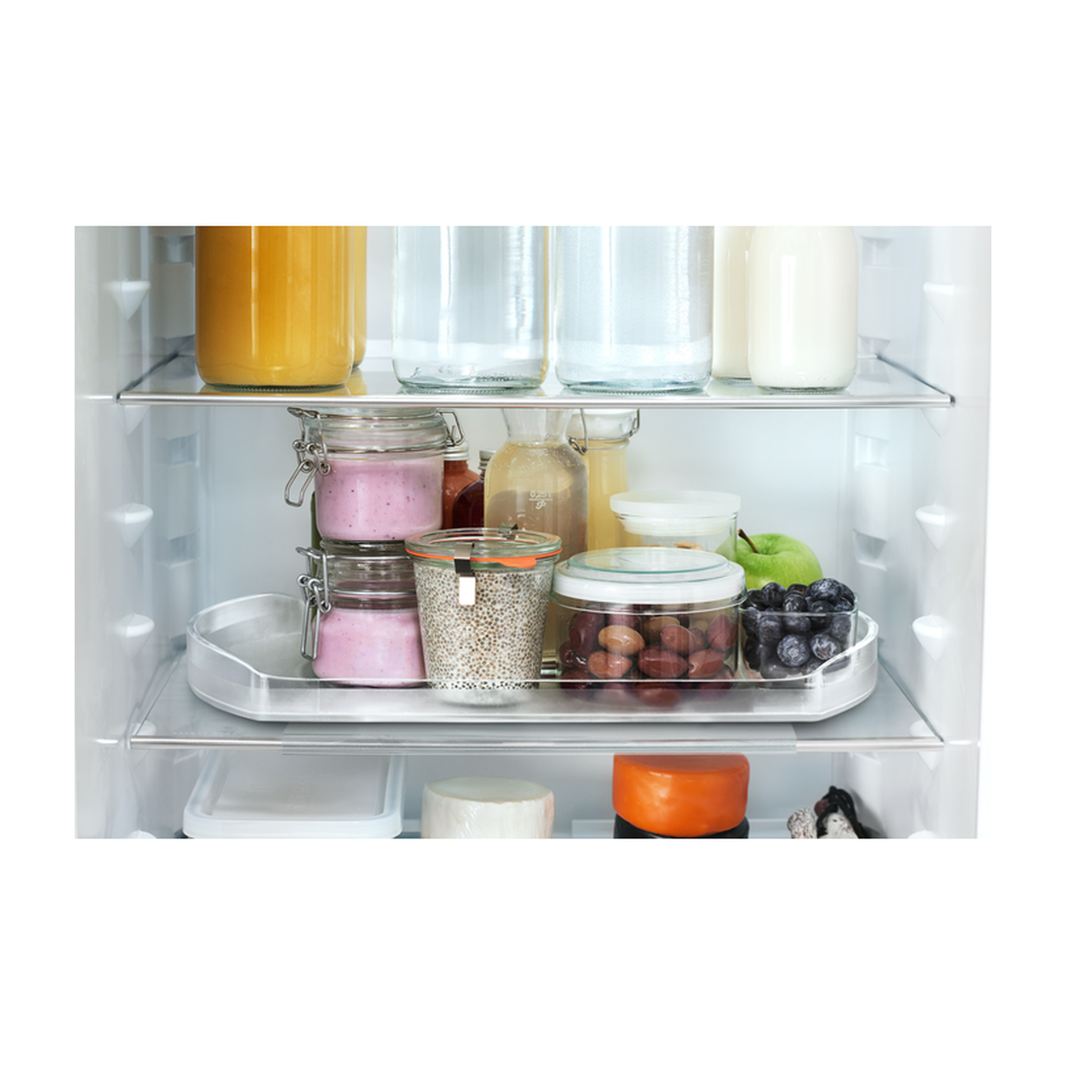 Barattoli pieni di succo, yogurt, cereali, olive, mirtilli, mela e formaggio in un frigorifero.