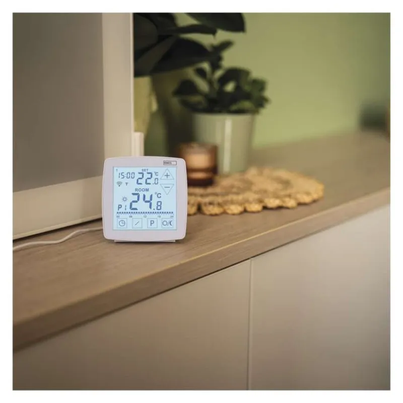Digitális termosztát fa felületen, növényekkel a háttérben.
