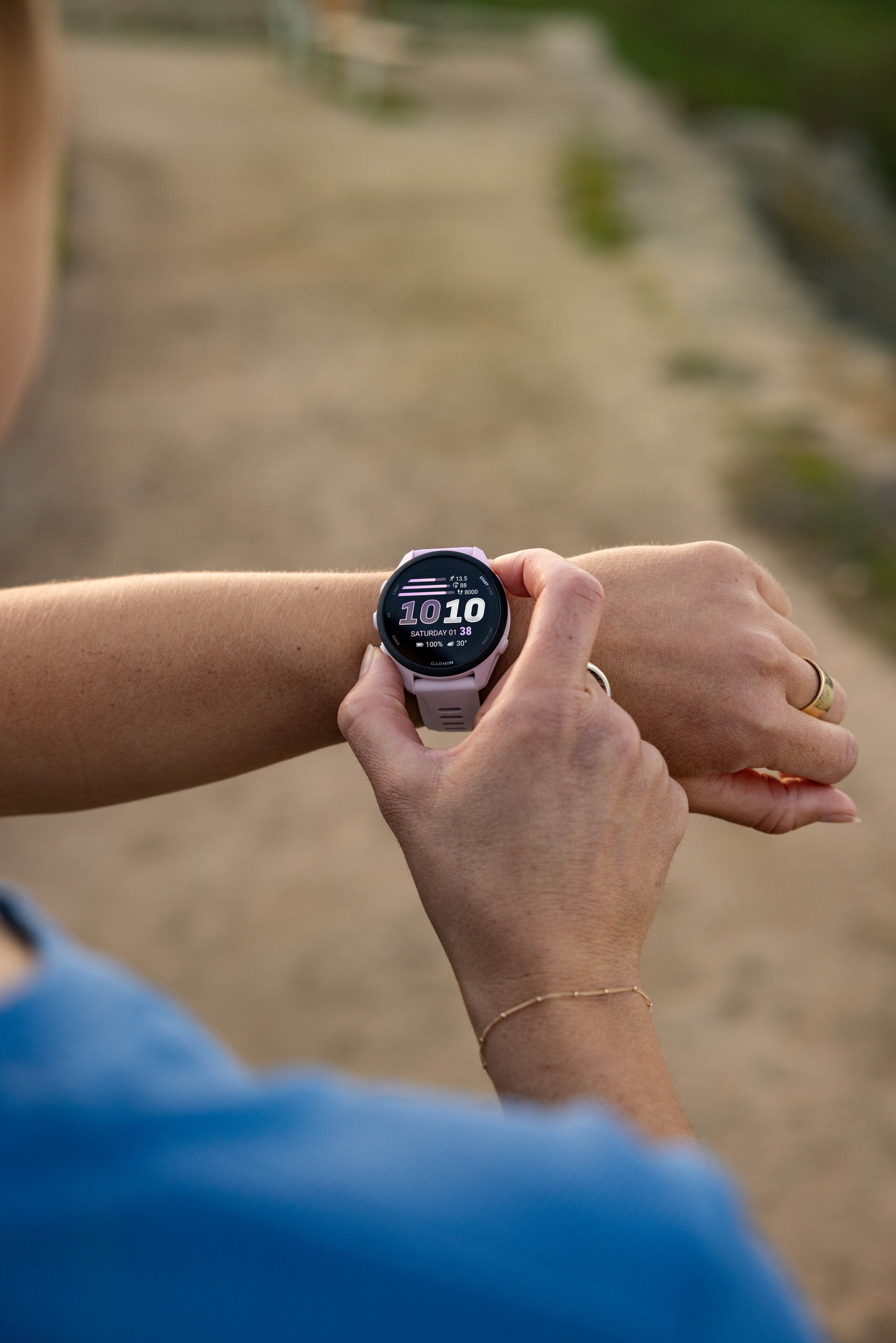 Eine Person in blauem Hemd prüft eine rosafarbene Smartwatch am Handgelenk.