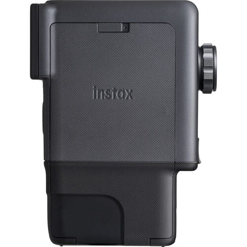 Szara kamera Instax z teksturowaną obudową i bocznym pokrętłem.