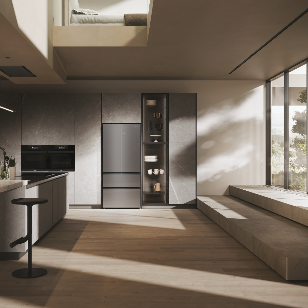 Cocina moderna con refrigerador gris, encimera, taburete y área de dormir elevada.
